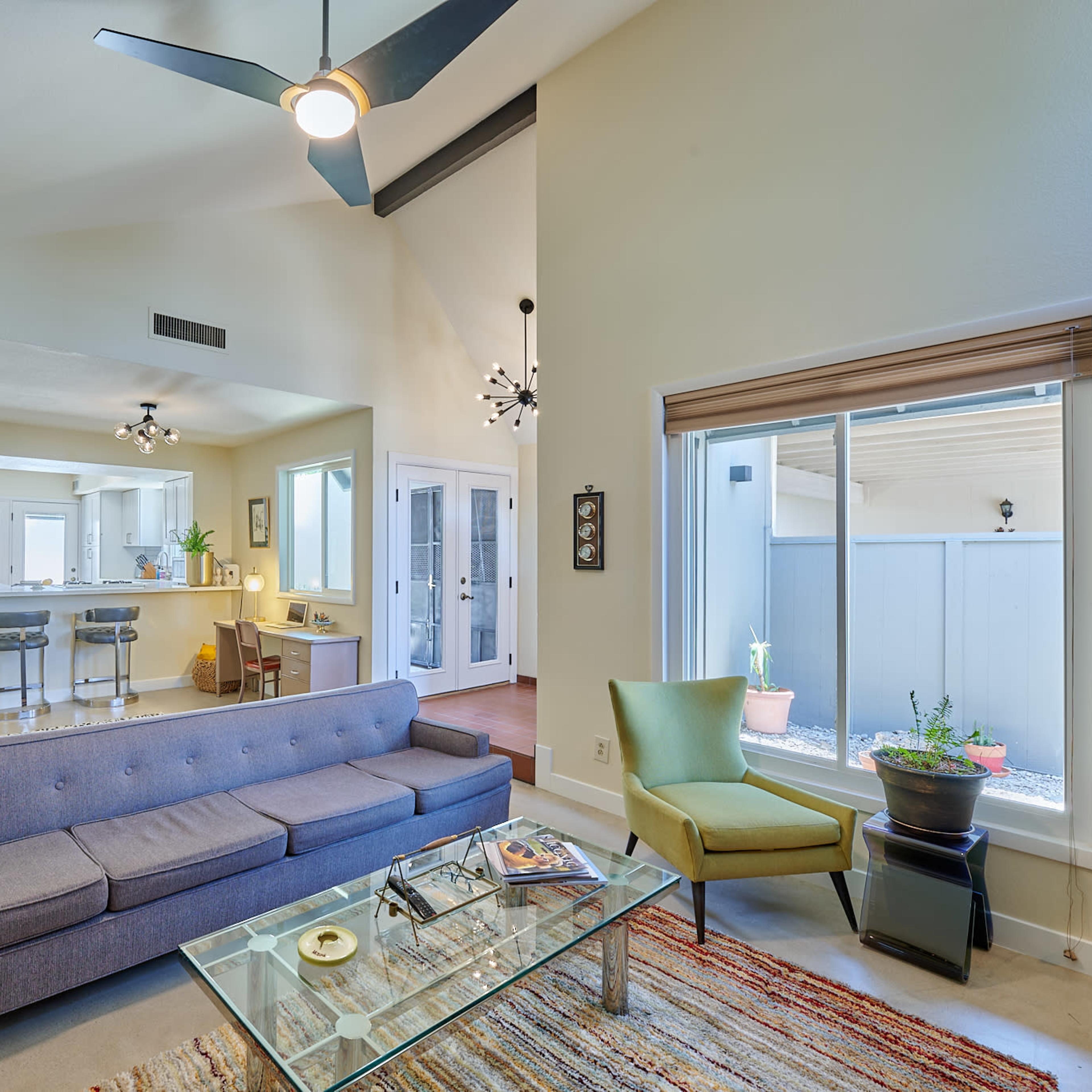 A modern living room with a gray sofa, a glass coffee table, and large windows that allow natural light to enter.