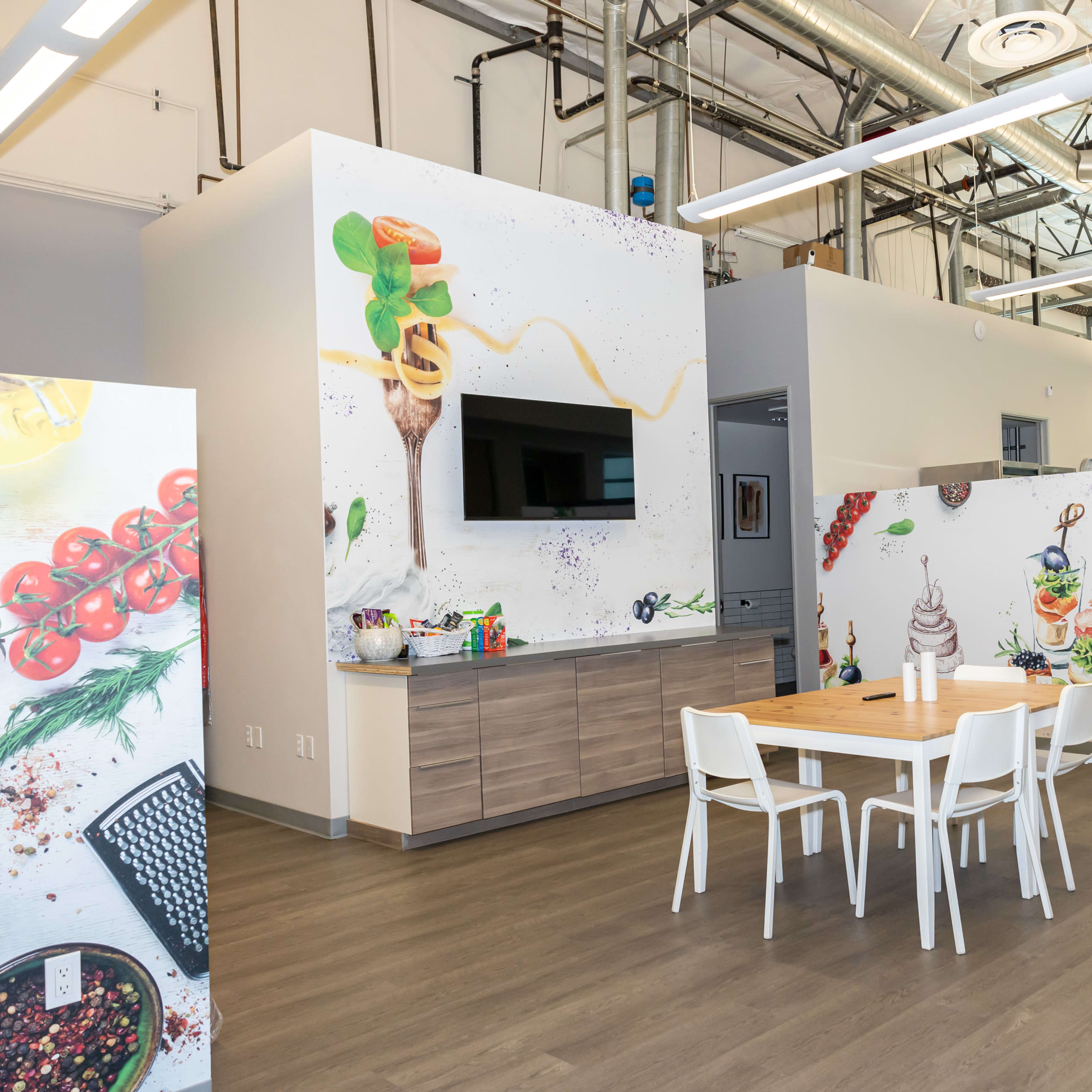 A modern kitchen area with a wooden dining table and walls decorated with colorful food illustrations.