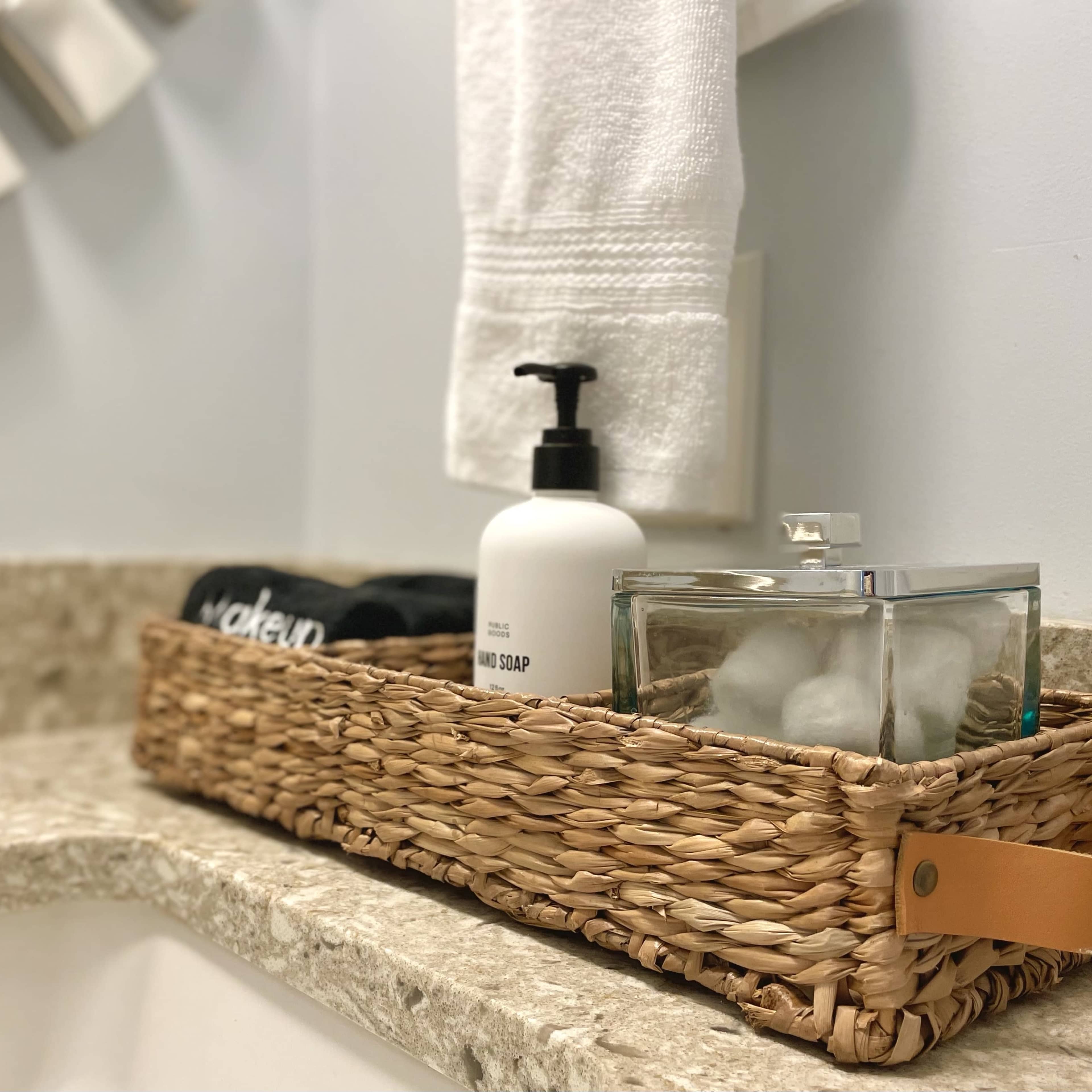 A woven basket containing toiletries is placed on a granite countertop next to a sink and mirror.