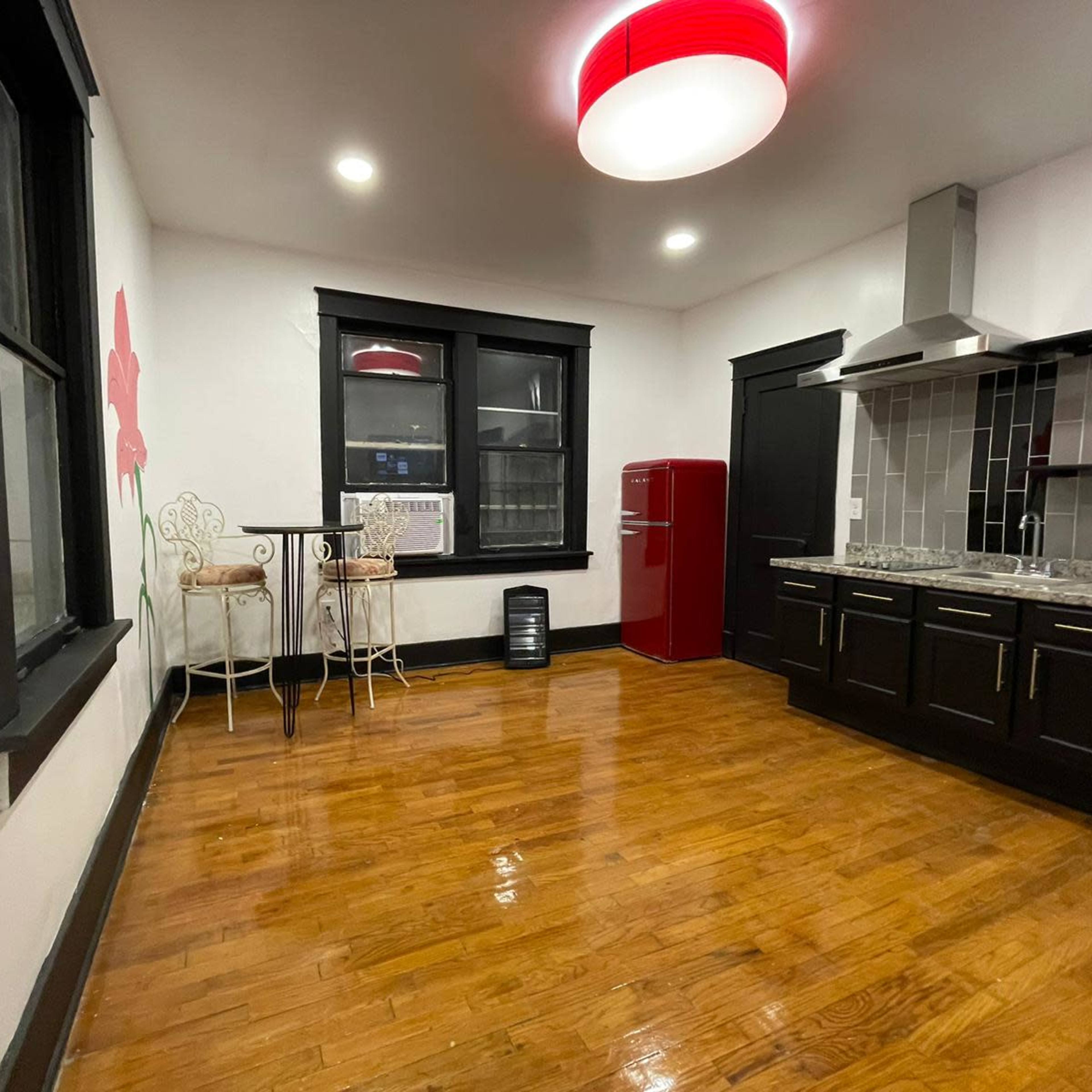 A modern kitchen features dark cabinetry, a red refrigerator, and a small dining area with two chairs against a wall.