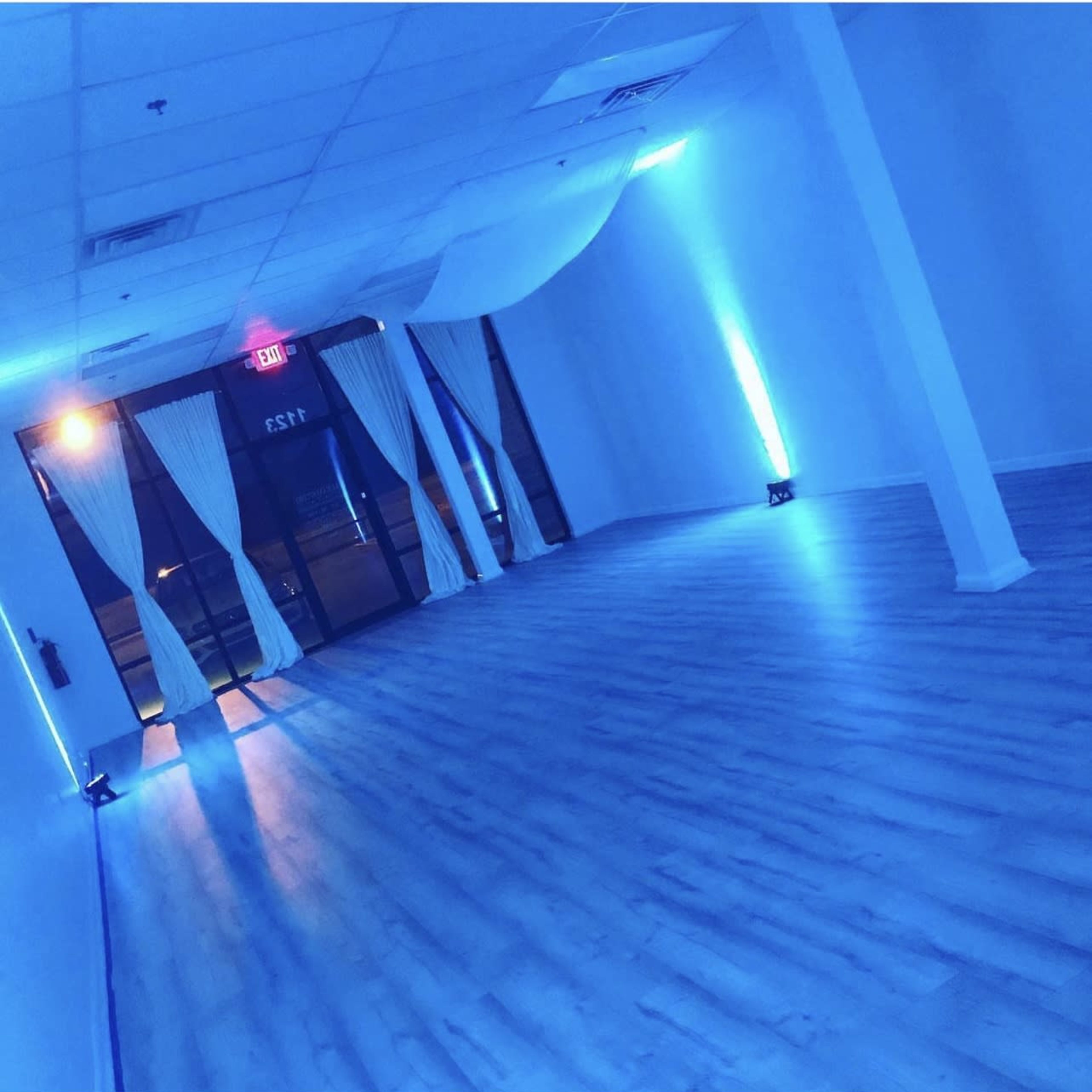 An empty room with blue lighting, white curtains, and a smooth wooden floor.
