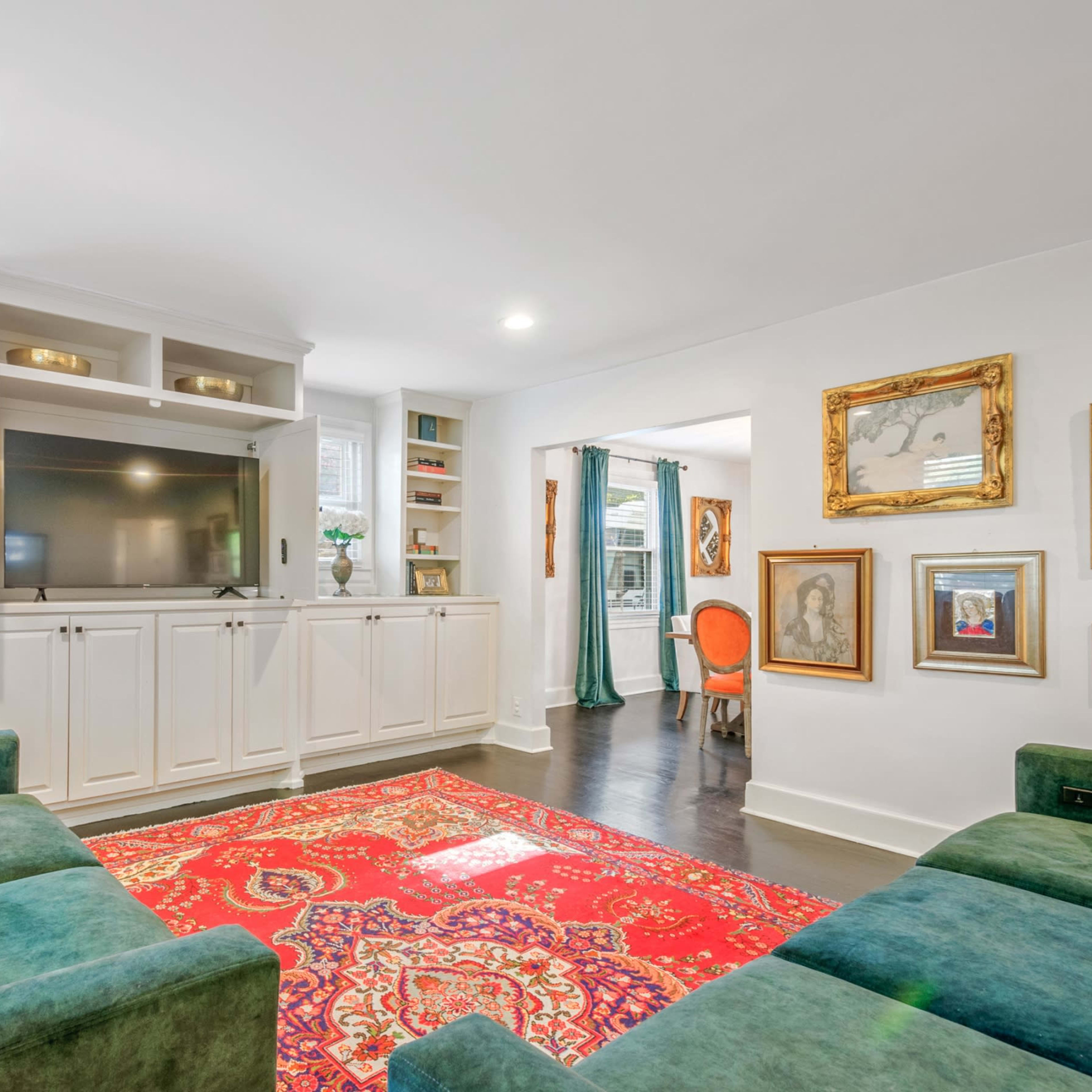 A living room features a green sectional sofa, a red patterned rug, and a built-in cabinet housing a television.