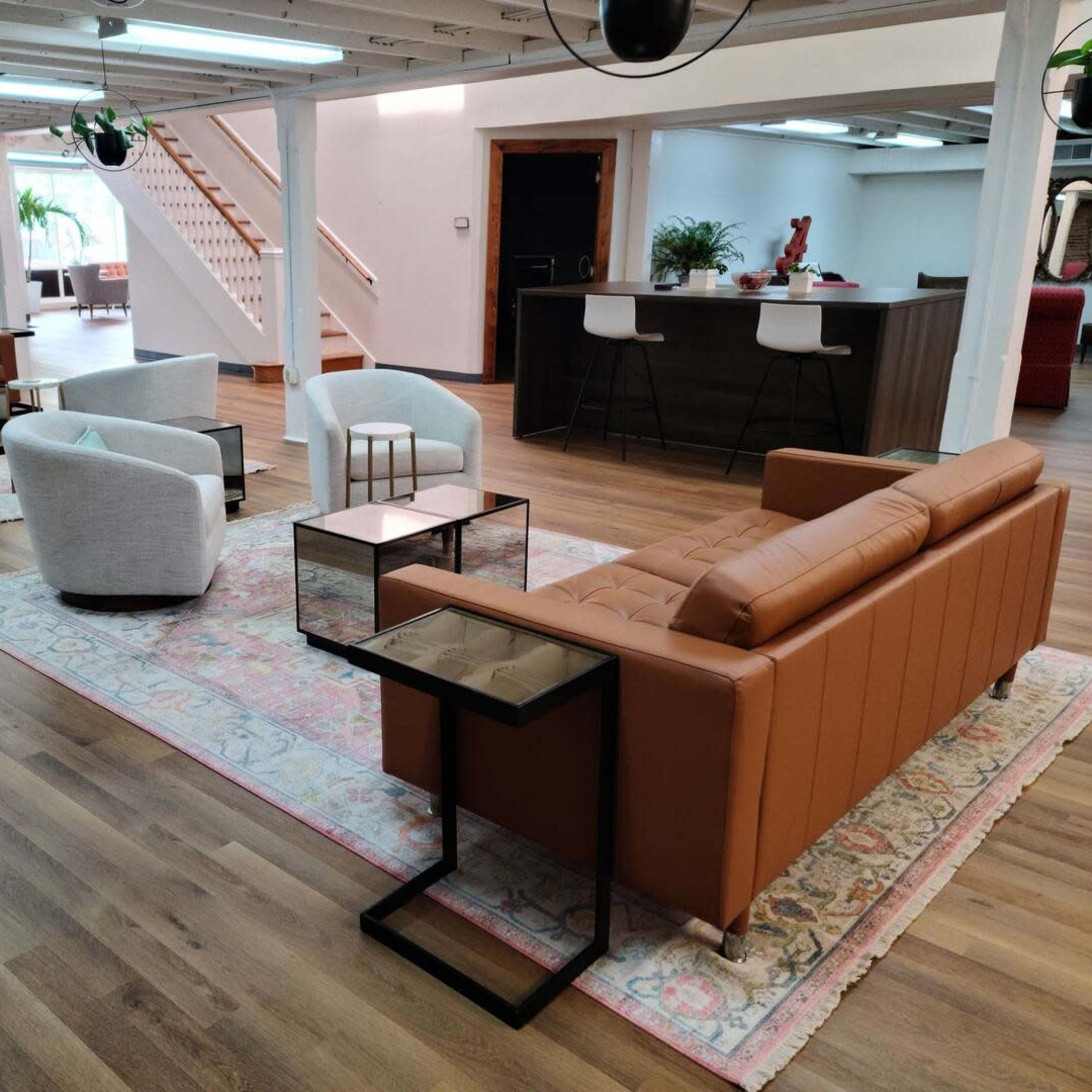 A spacious interior with several modern seating arrangements, including brown leather sofas and circular armchairs, arranged around small black side tables on a decorative rug.