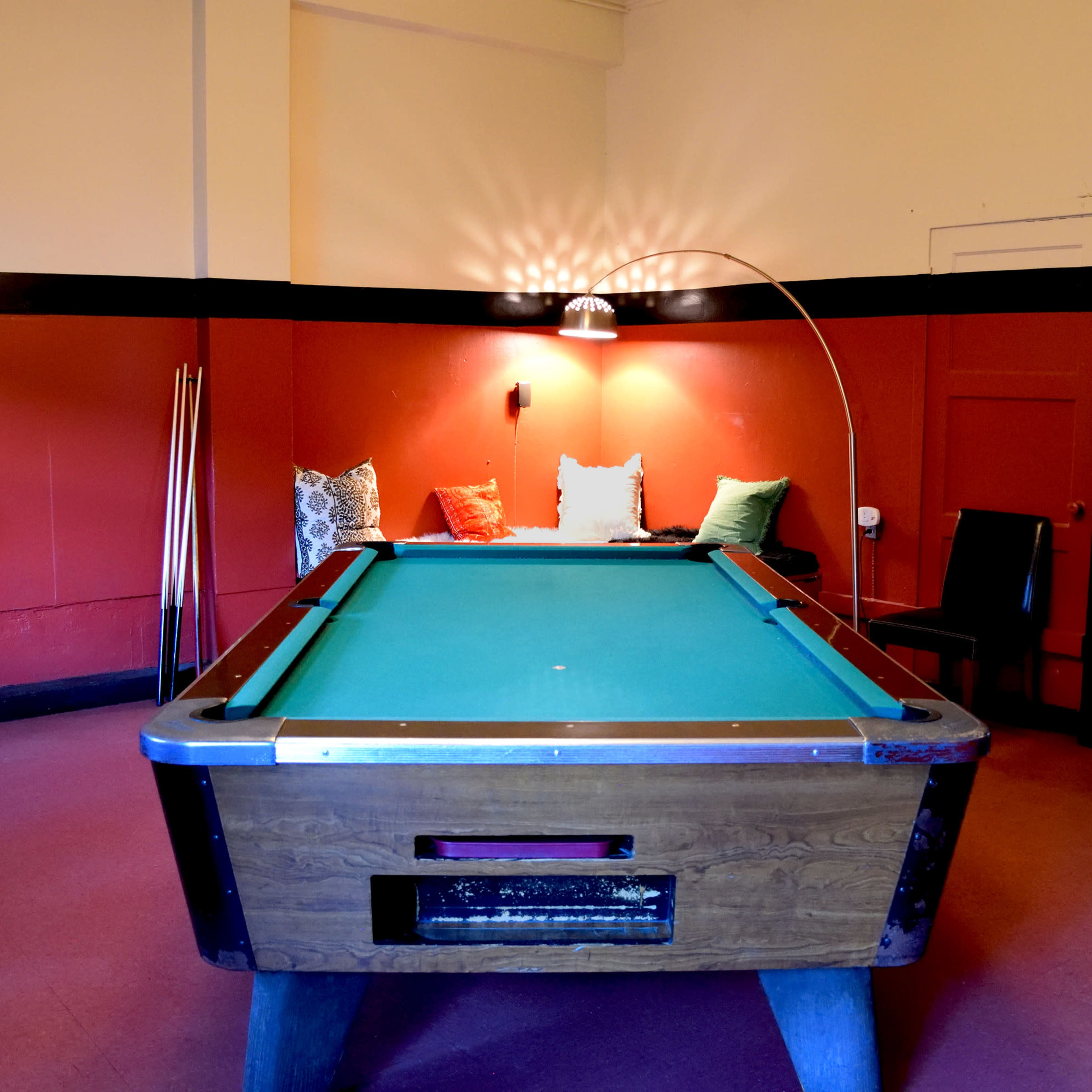 A pool table positioned centrally in a room with red walls and a small seating area in the background.