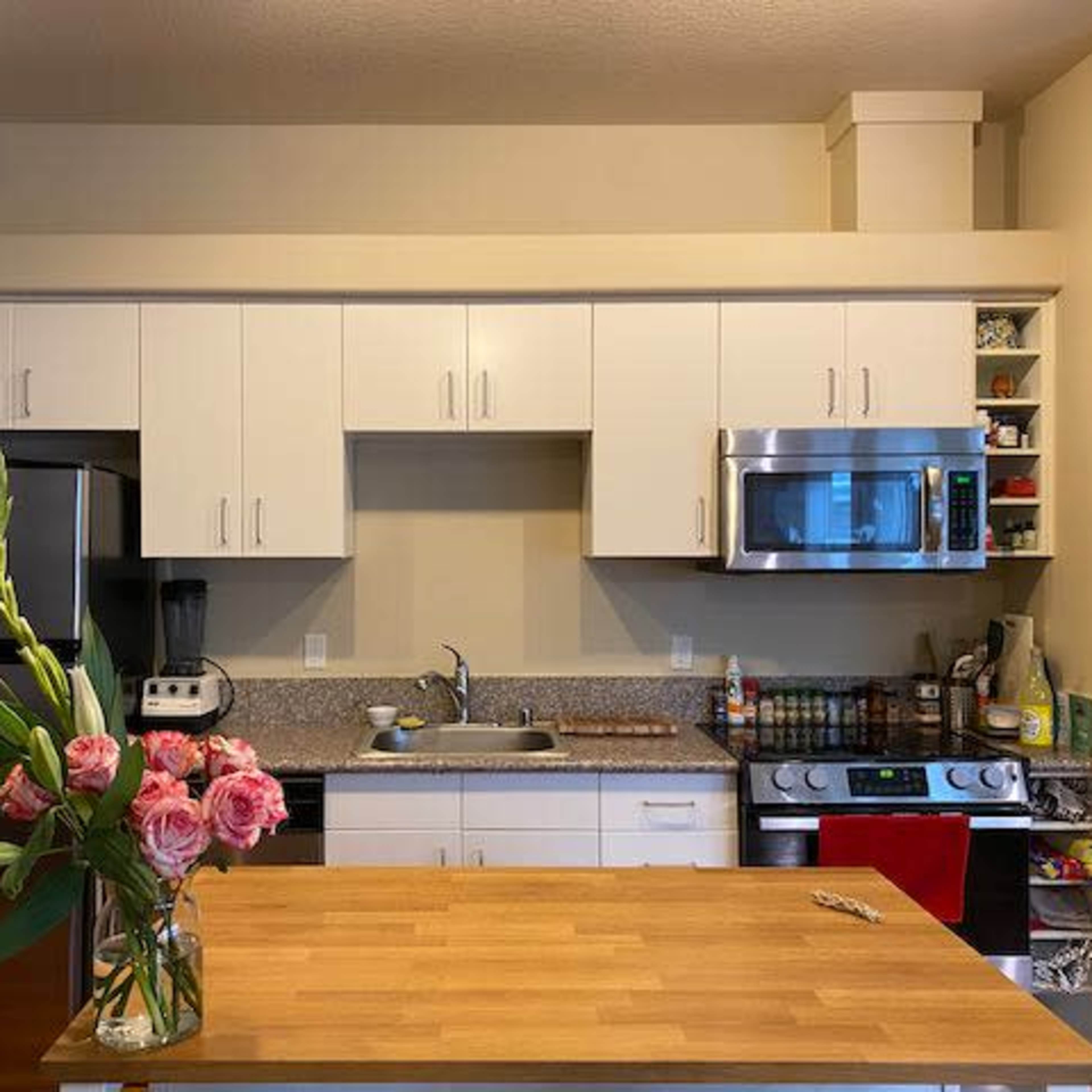 A clean kitchen features white cabinetry, stainless steel appliances, a central wooden island, and a vase of pink flowers.