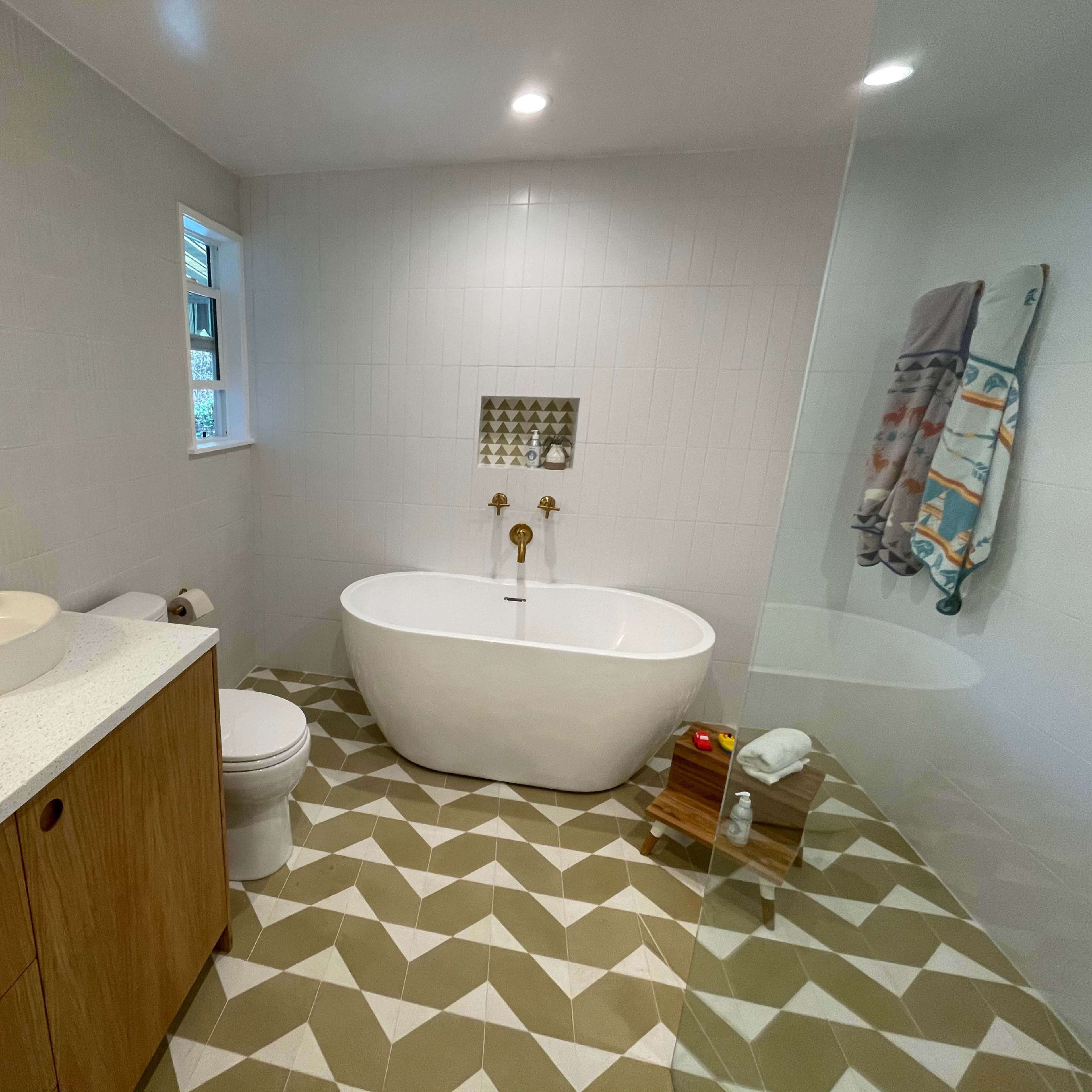 A modern bathroom featuring a freestanding bathtub, a wall-mounted sink with a mirror, and patterned floor tiles.
