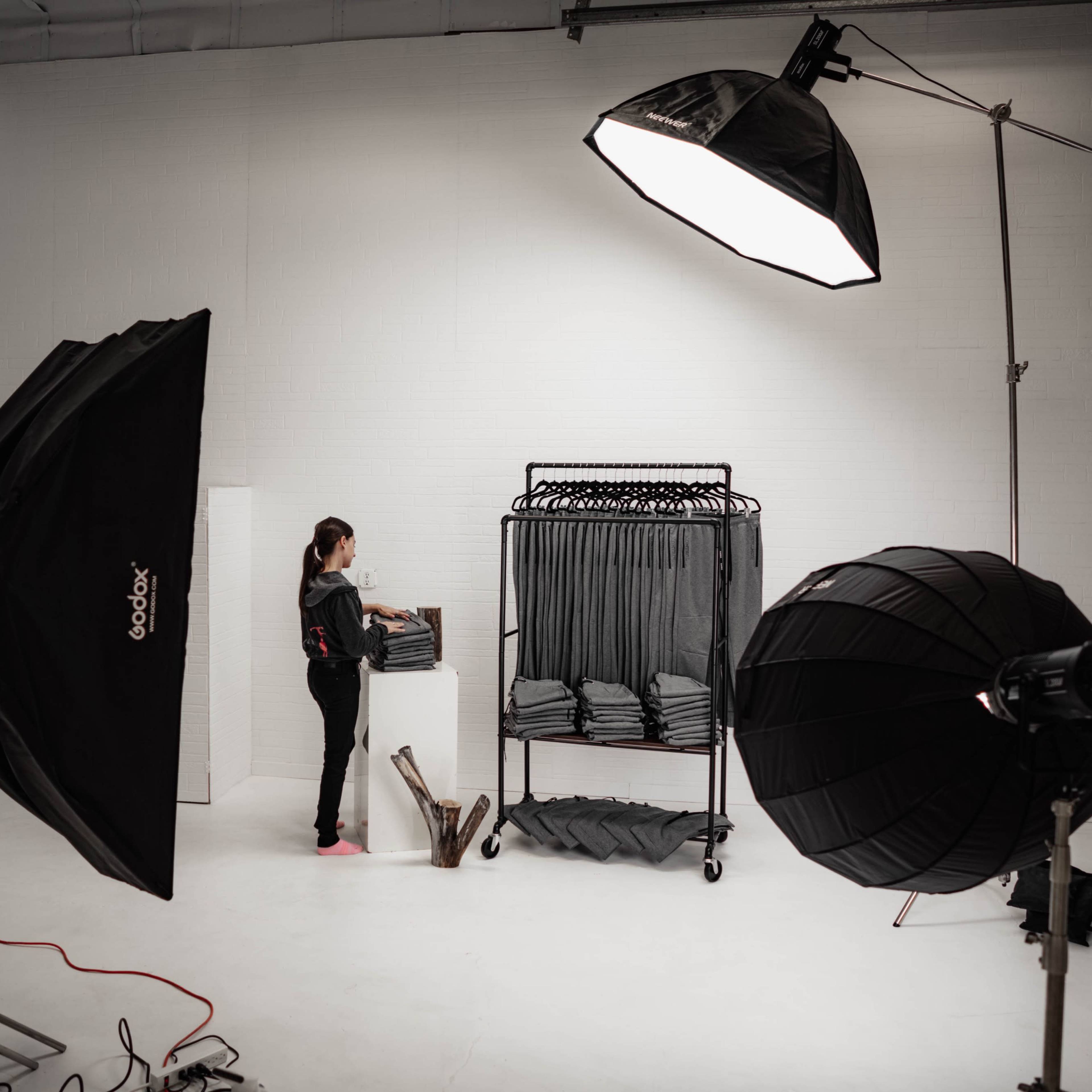 A woman organizes clothing on a rack in a photography studio equipped with several lighting setups.