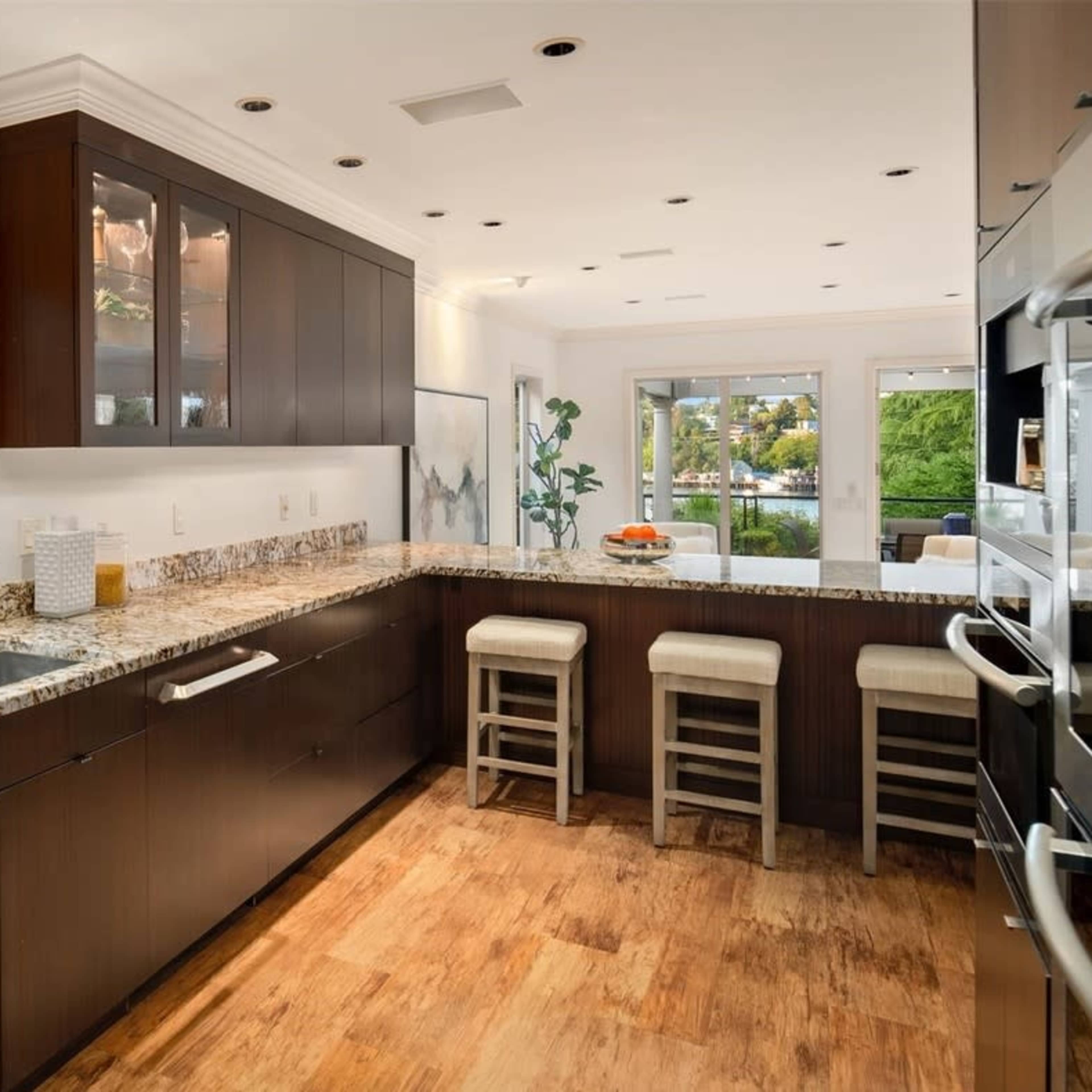 A modern kitchen features dark cabinetry, a granite countertop, and bar seating, with windows providing views of the outdoors.