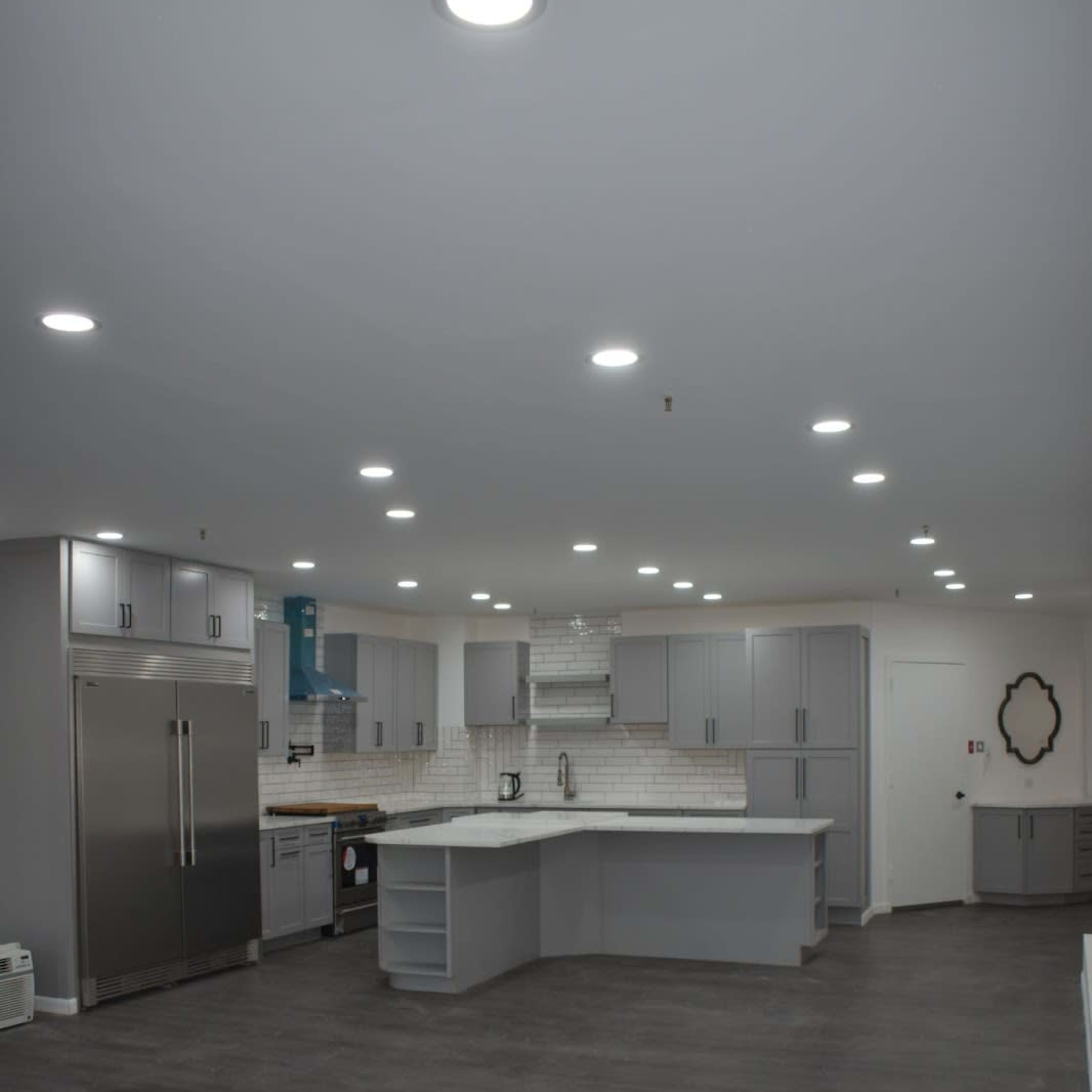 A spacious kitchen with gray cabinetry, an island countertop, and modern appliances set on dark wooden flooring.