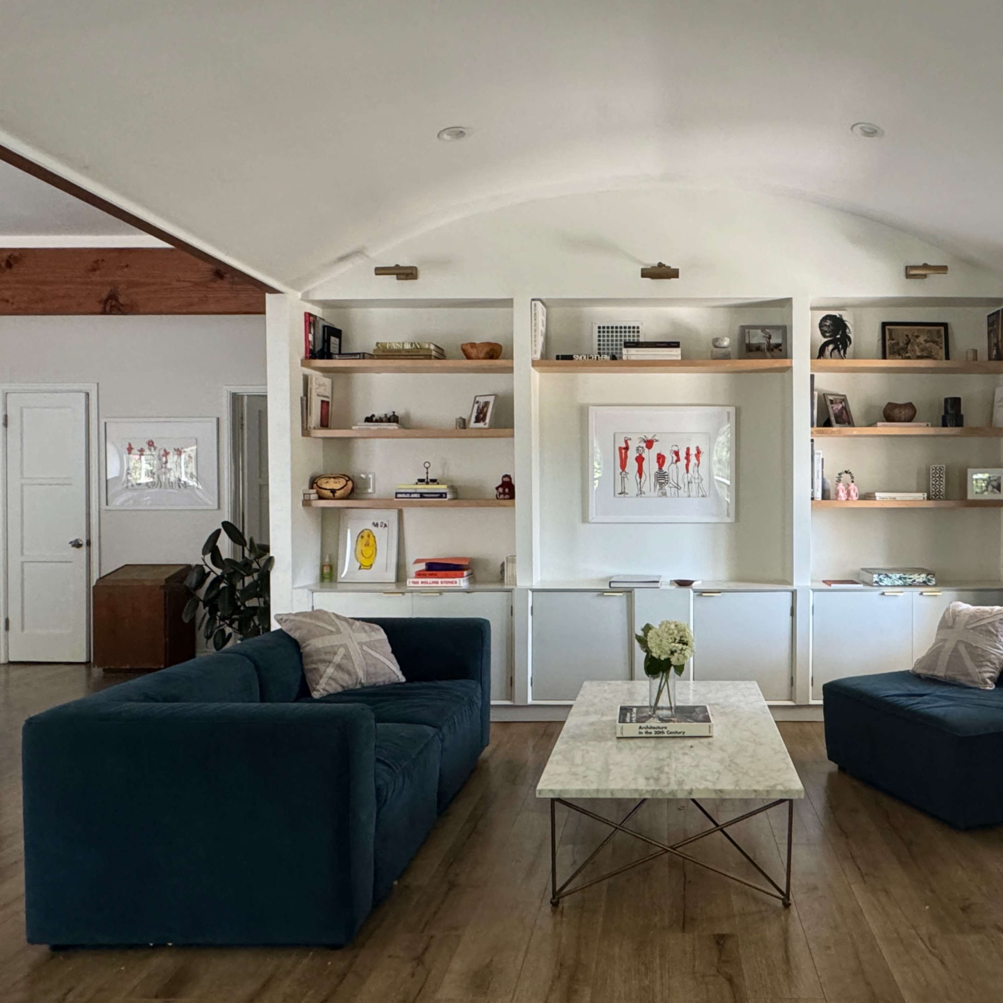 A modern living room with two dark blue sofas facing a marble coffee table, flanked by built-in shelves displaying various decorative items.