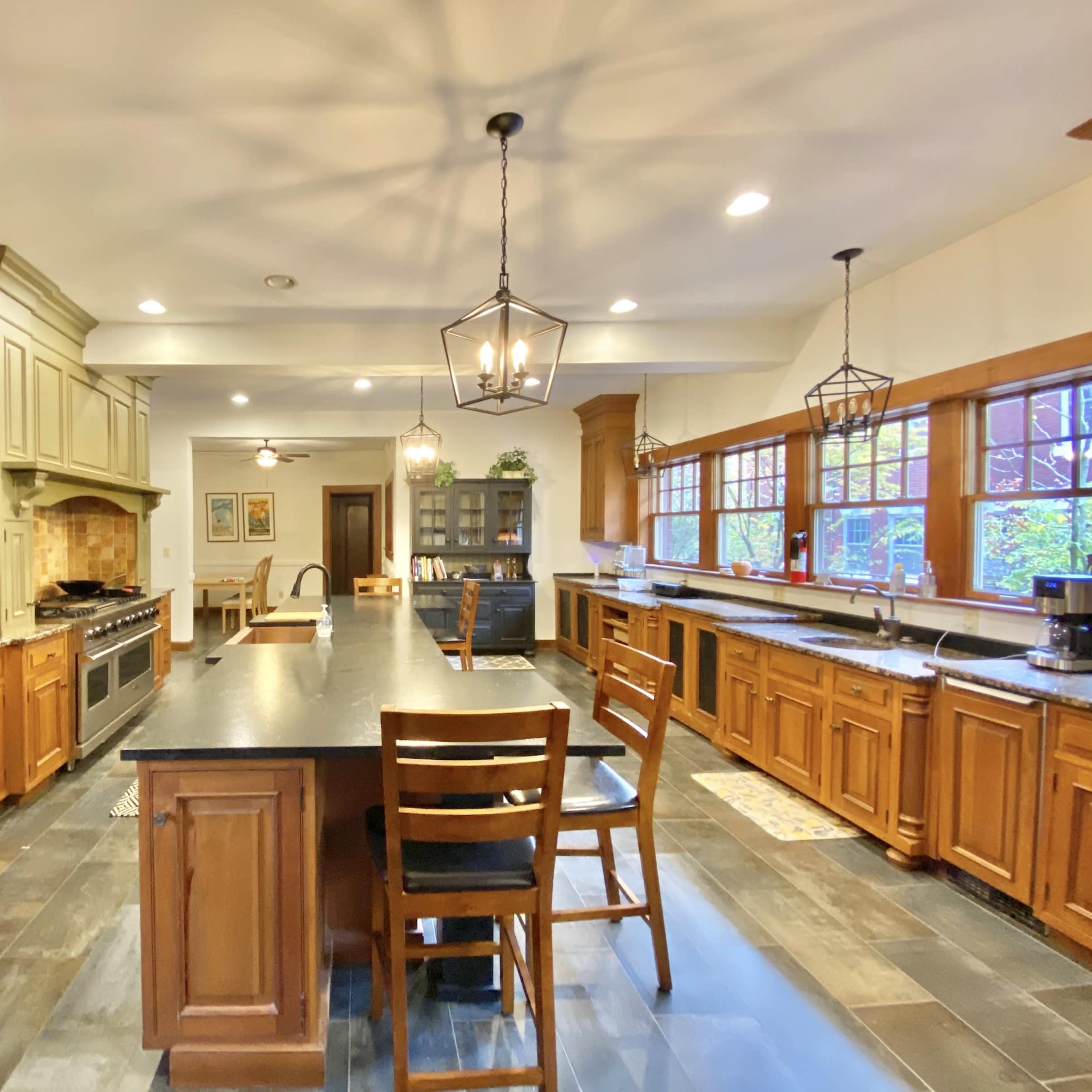 A spacious kitchen with wooden cabinetry, a large island with seating, and multiple windows allowing natural light.