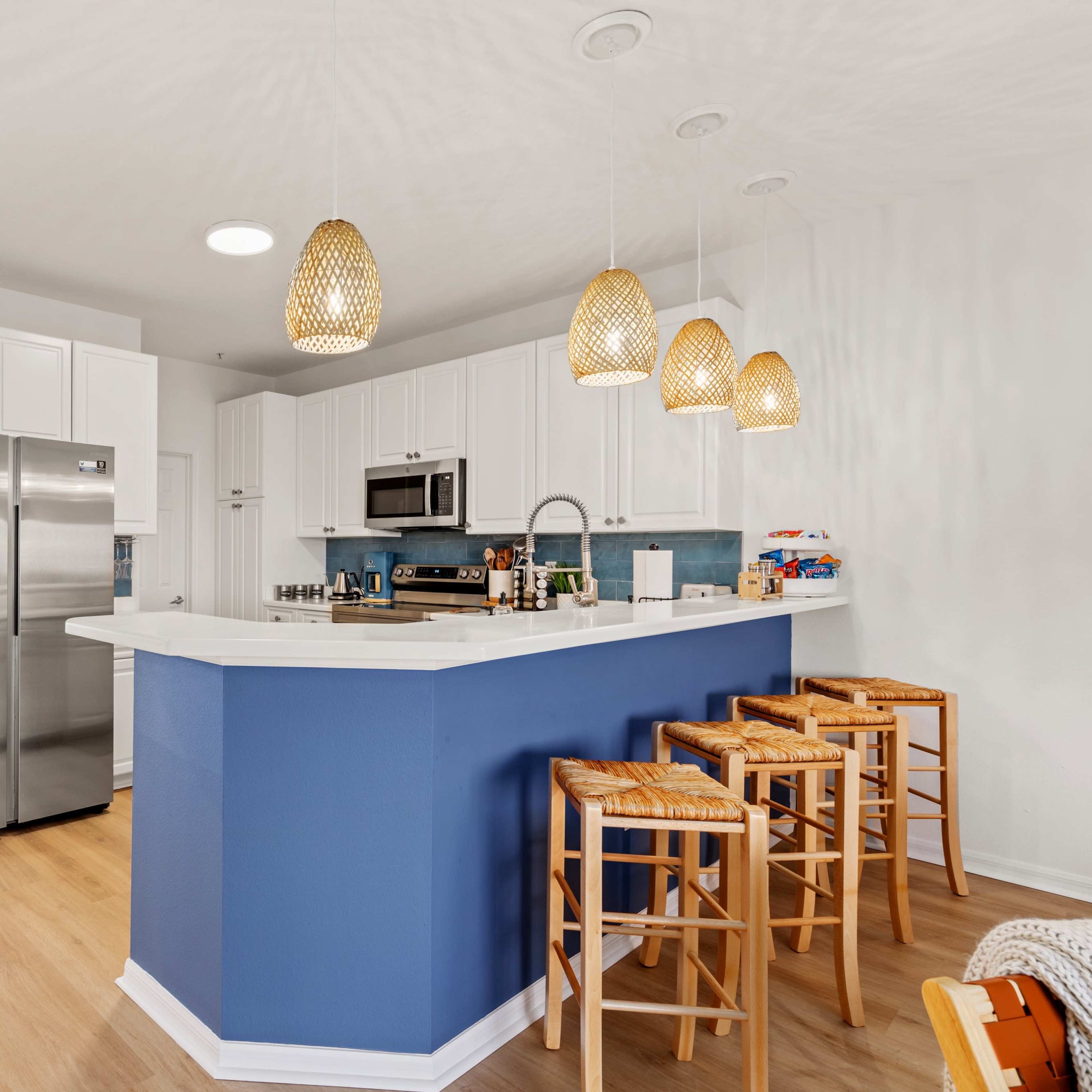 A modern kitchen features white cabinets, stainless steel appliances, a blue accent wall, and three wooden bar stools at the island.
