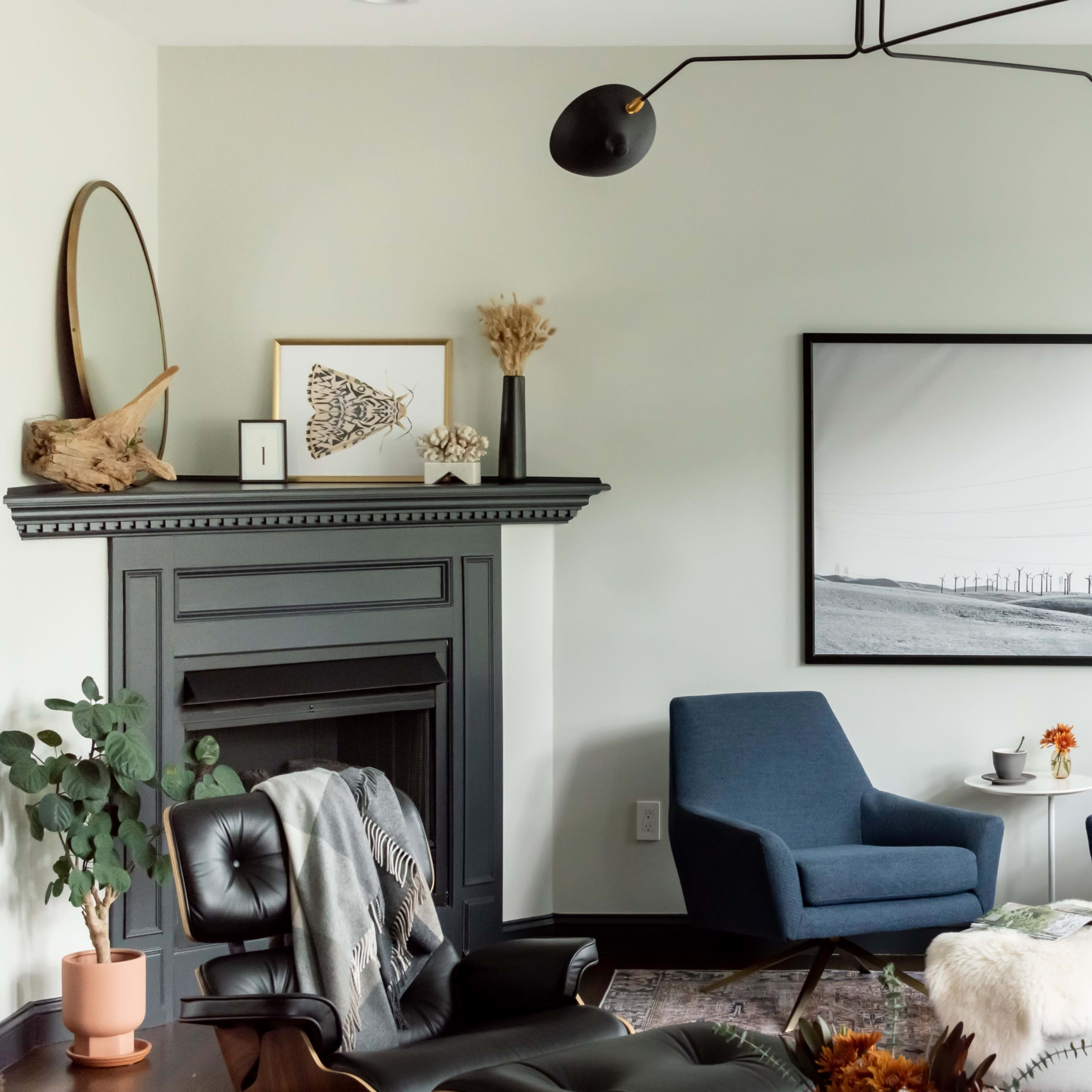 A modern living room features two blue armchairs facing a black-and-white landscape photograph, with a fireplace adorned with decorative items and a plant in the corner.