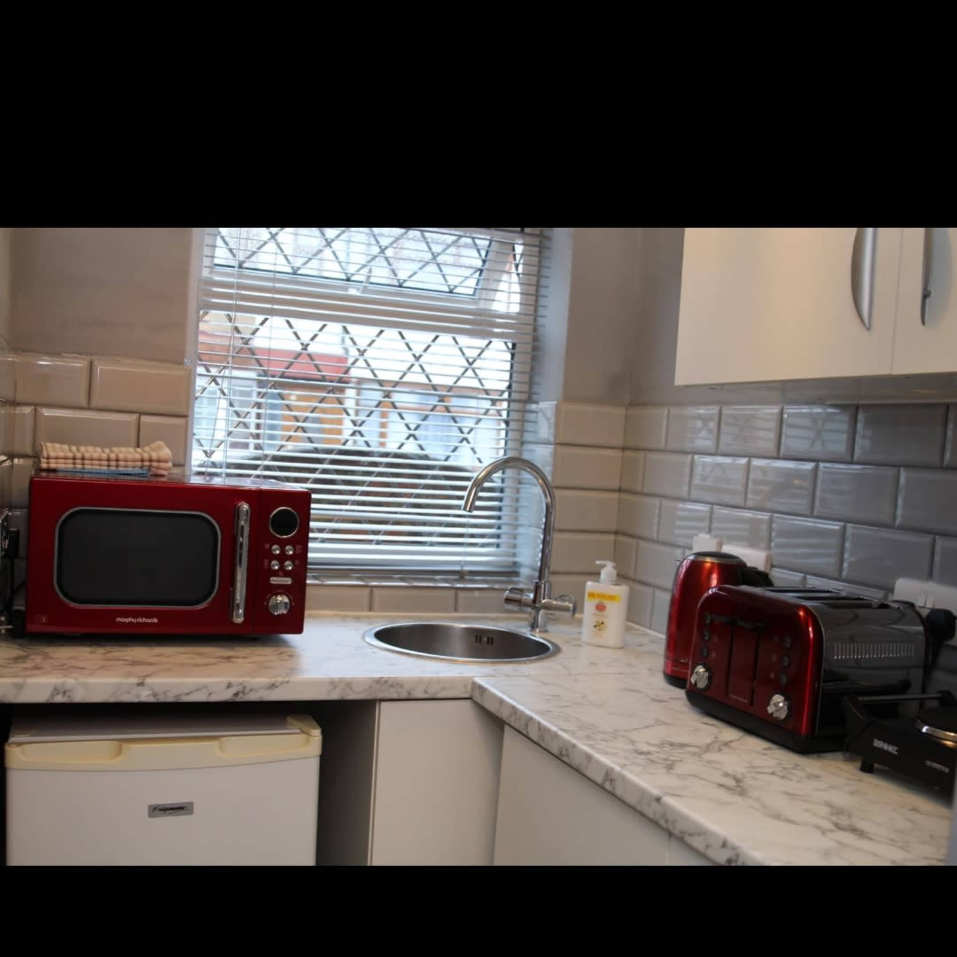 A kitchen with a red microwave and toaster on a marble countertop, a sink, and a window with a grid pattern above it.