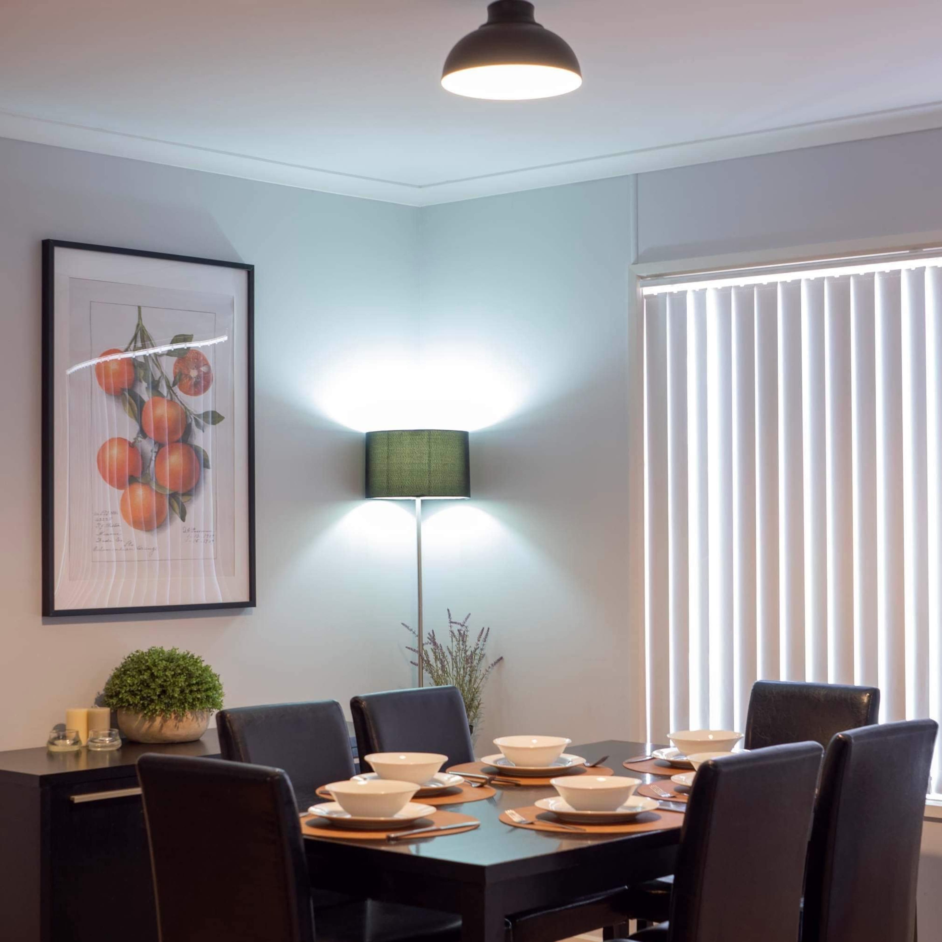 A dining area features a table set for six with bowls and a framed artwork of oranges on the wall.