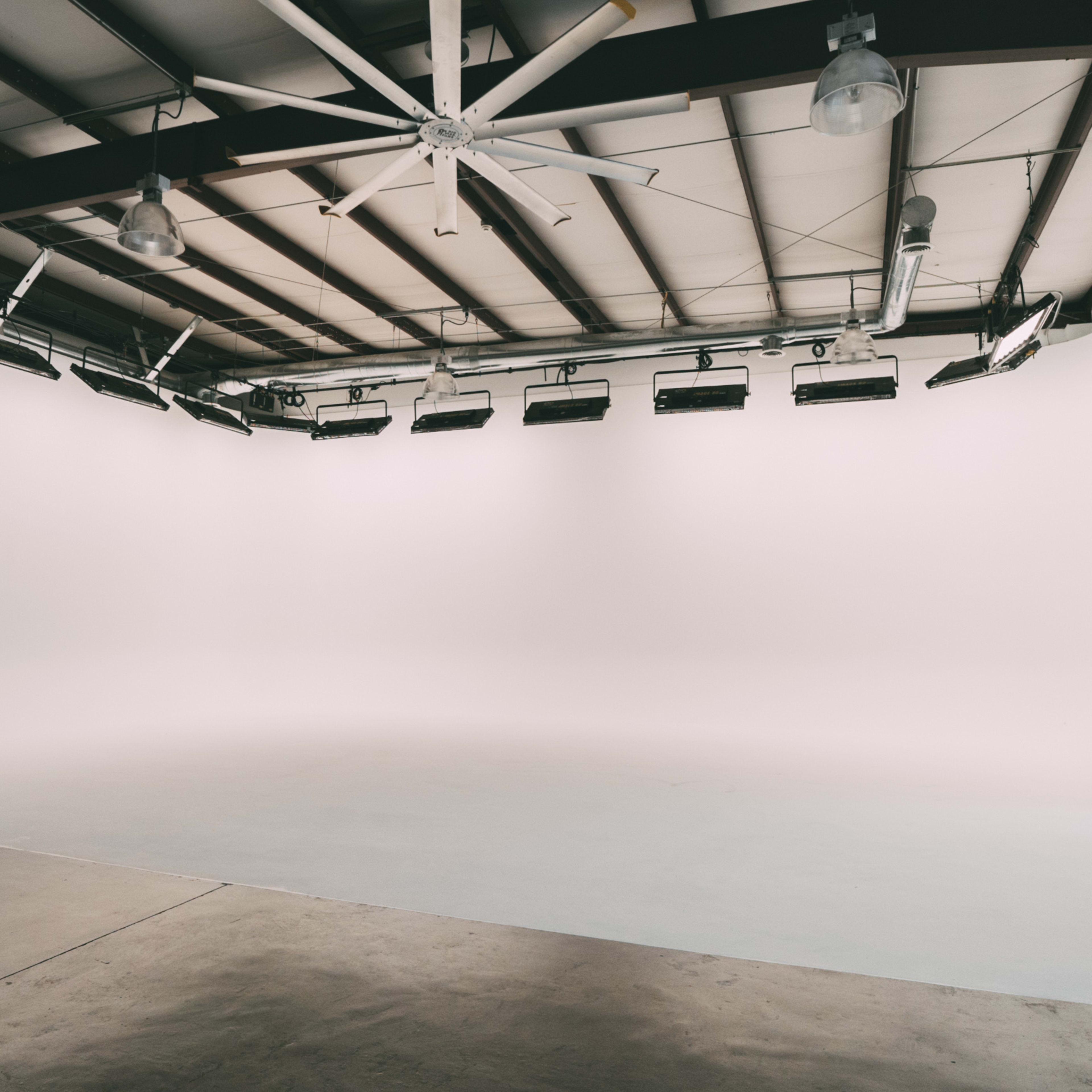 A spacious, empty studio with a seamless white backdrop and overhead lighting.