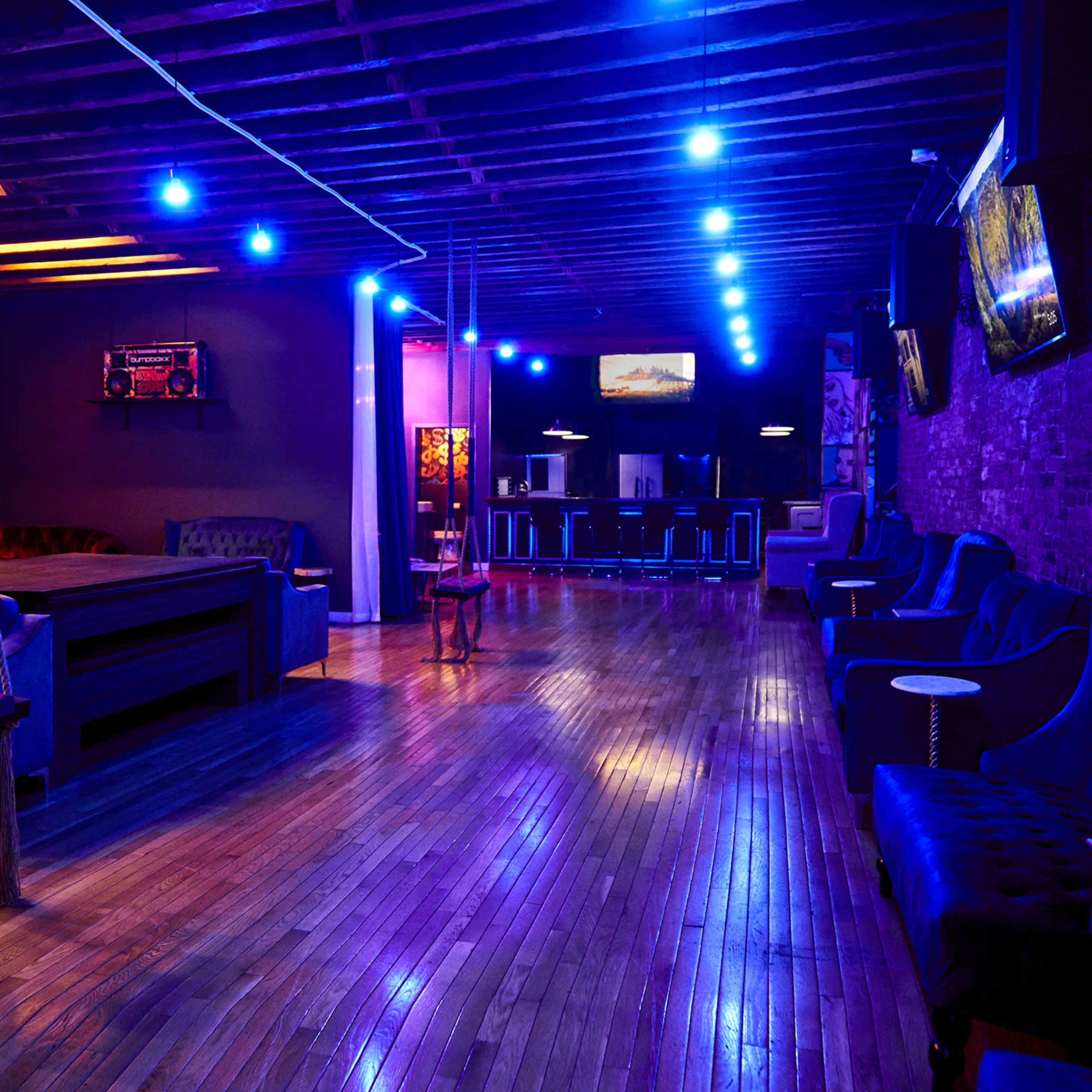A dimly lit lounge area with blue lighting, featuring a mix of seating options and wooden floors.
