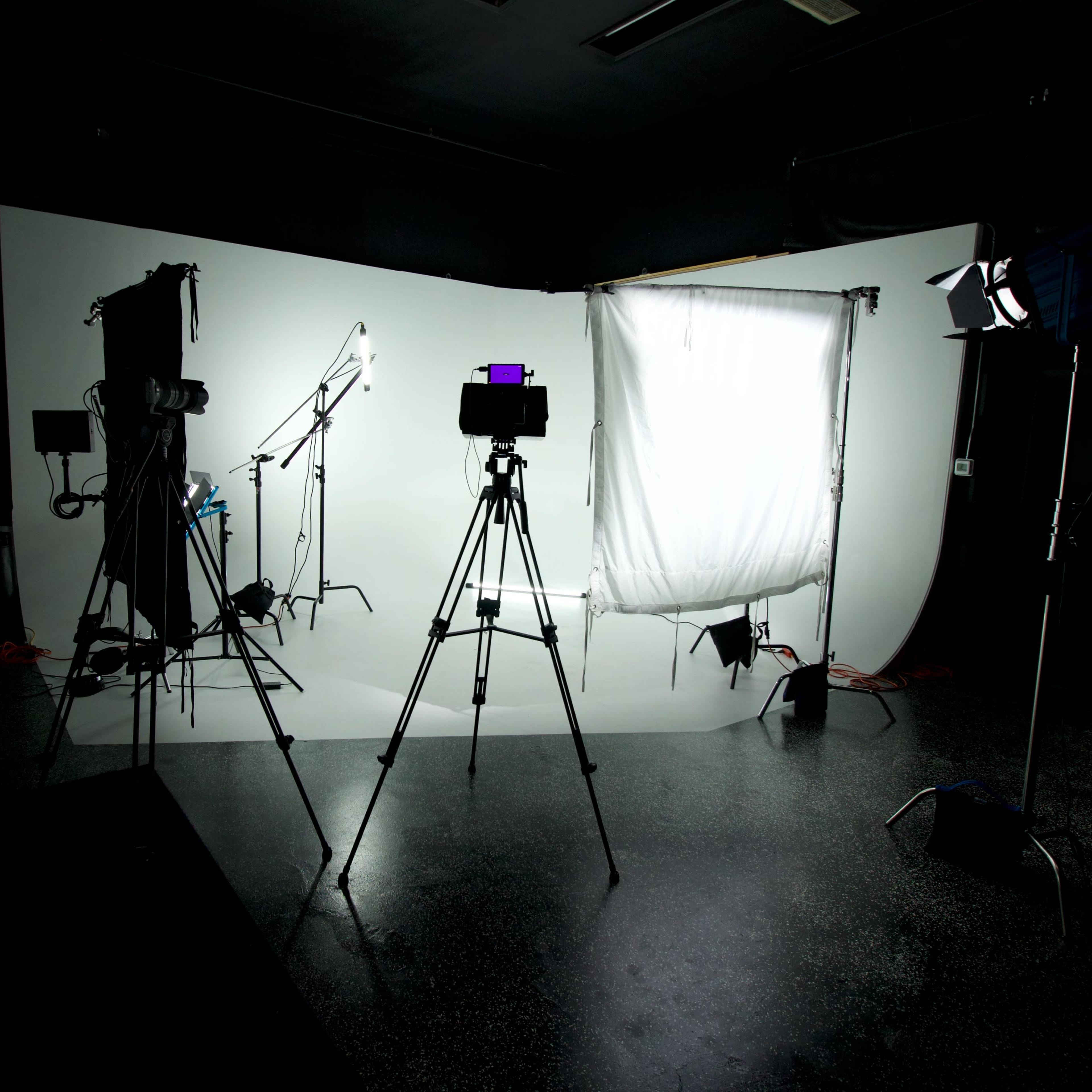 A photography studio setup with multiple tripods, lights, and a backdrop arranged against a curved white wall.