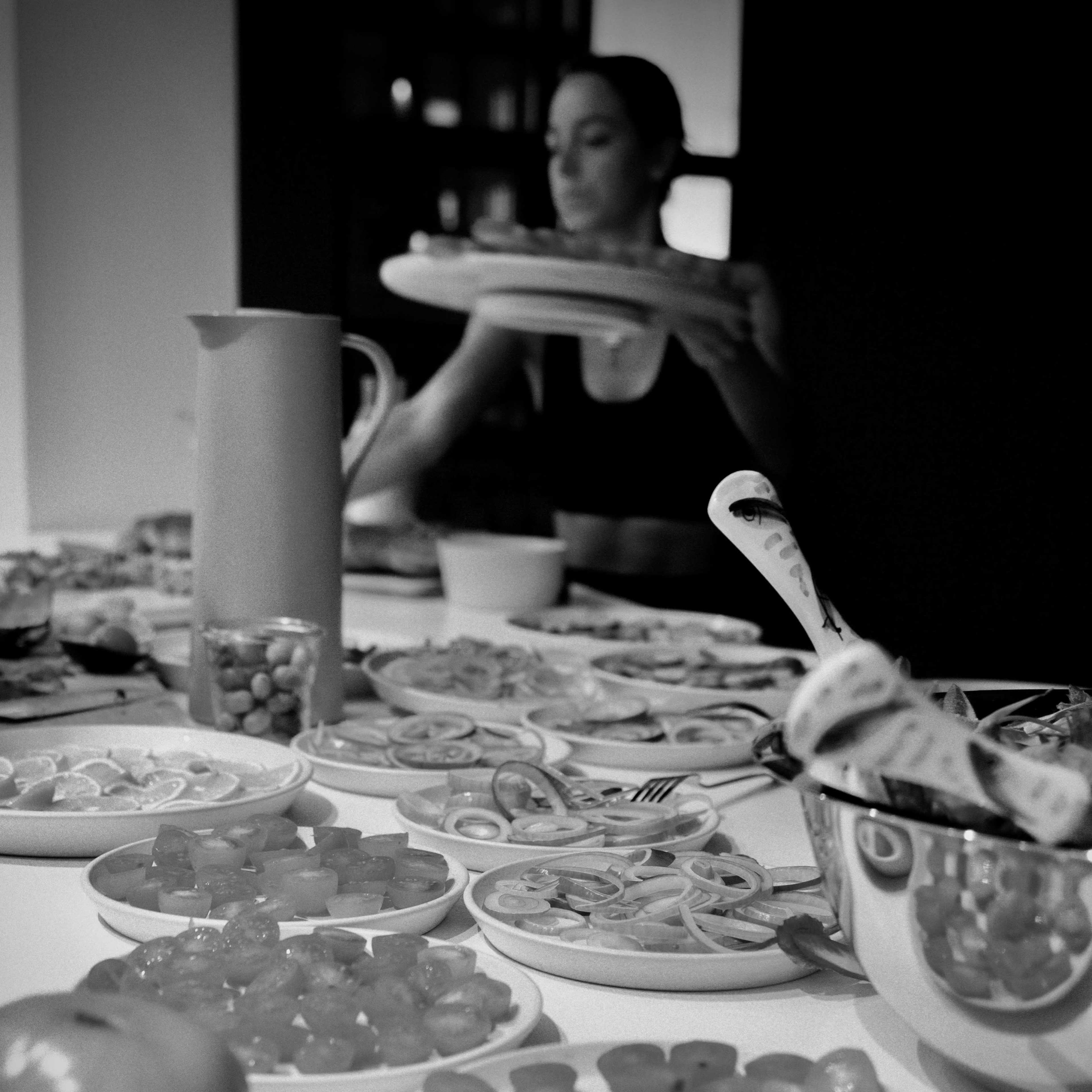 A woman arranges food items on a table filled with various dishes, including fruits and colorful snacks.