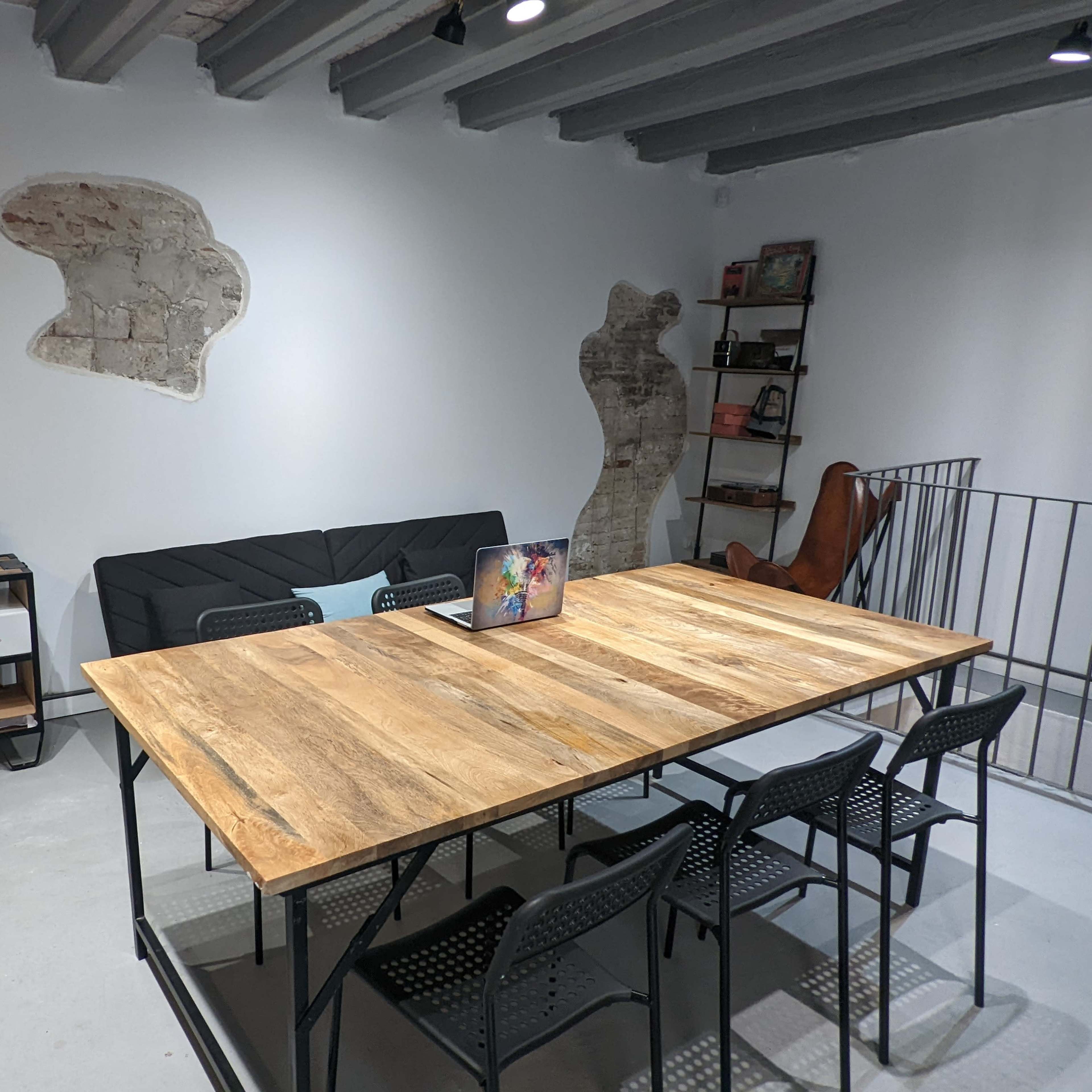 A modern meeting room featuring a large wooden table with black chairs, a couch, a shelf with books, and an abstract wall design.