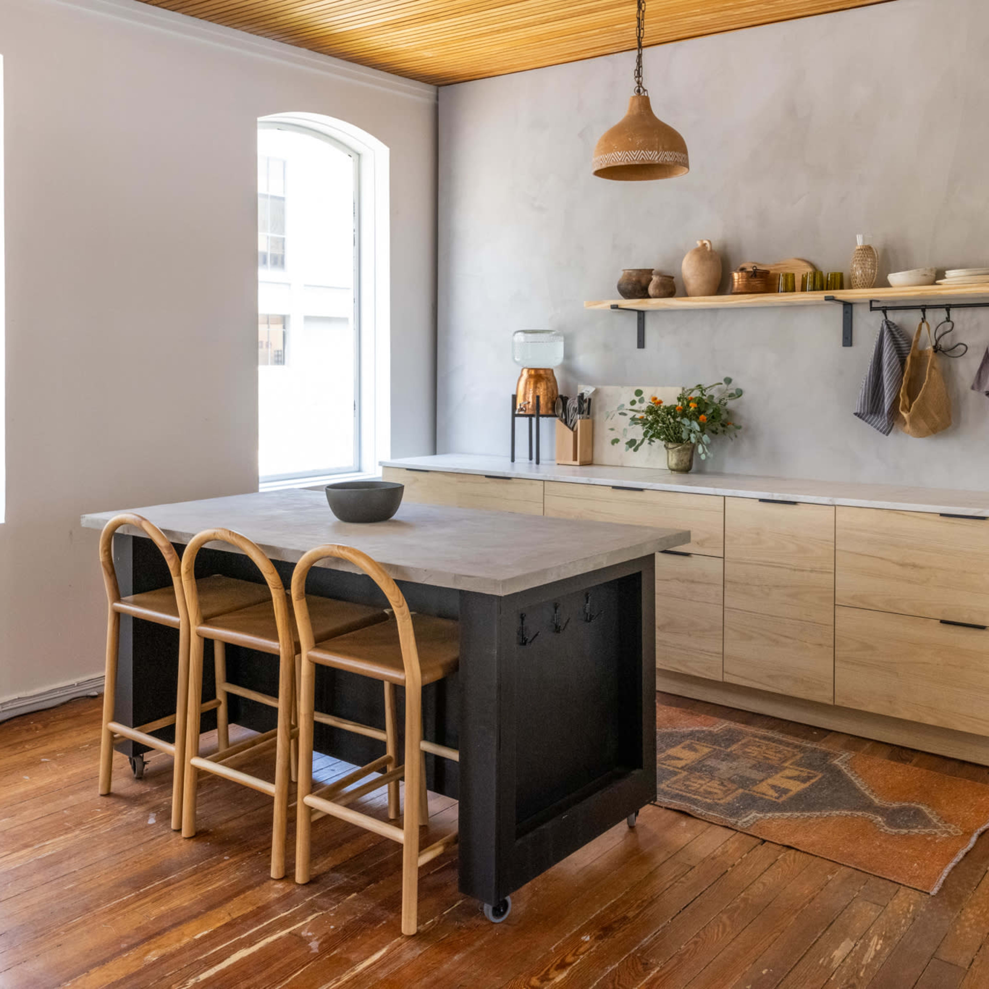 The kitchen features a wood countertop island with three rattan stools, light wood cabinetry, and a large window providing natural light.