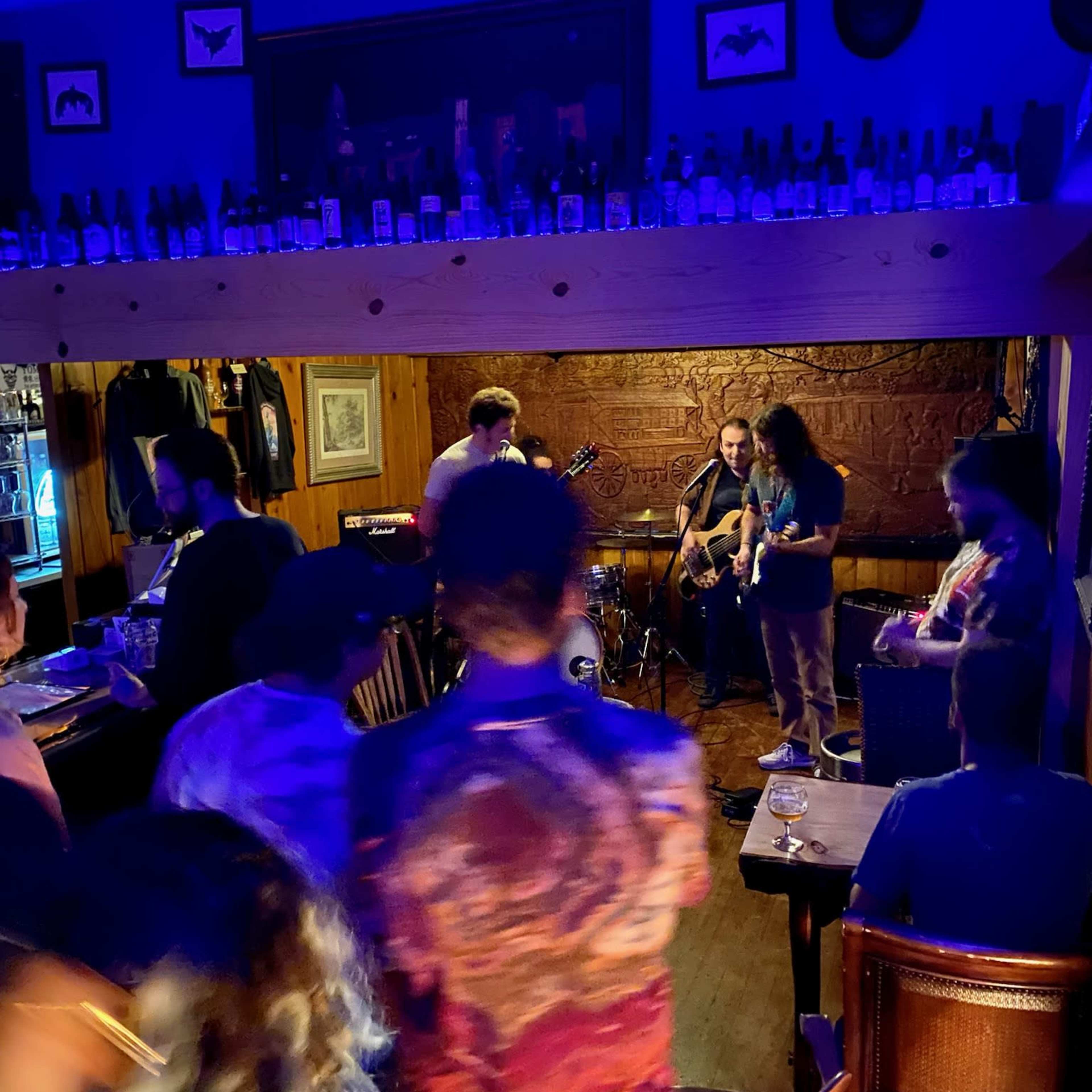 A band performs on a small stage in a dimly lit bar while patrons gather and enjoy the live music.