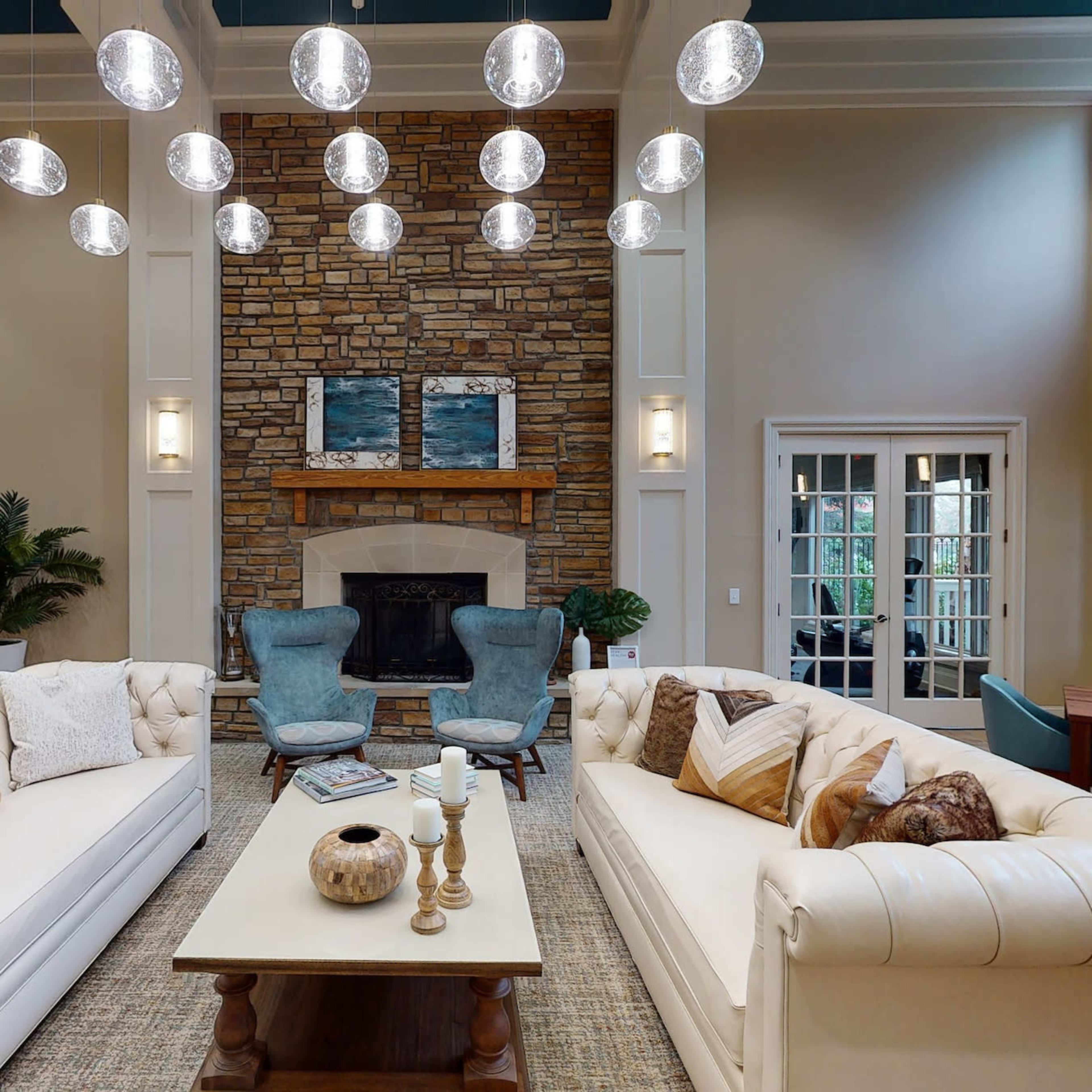 A spacious living area features two white tufted sofas, a stone fireplace, and a collection of modern hanging light fixtures.