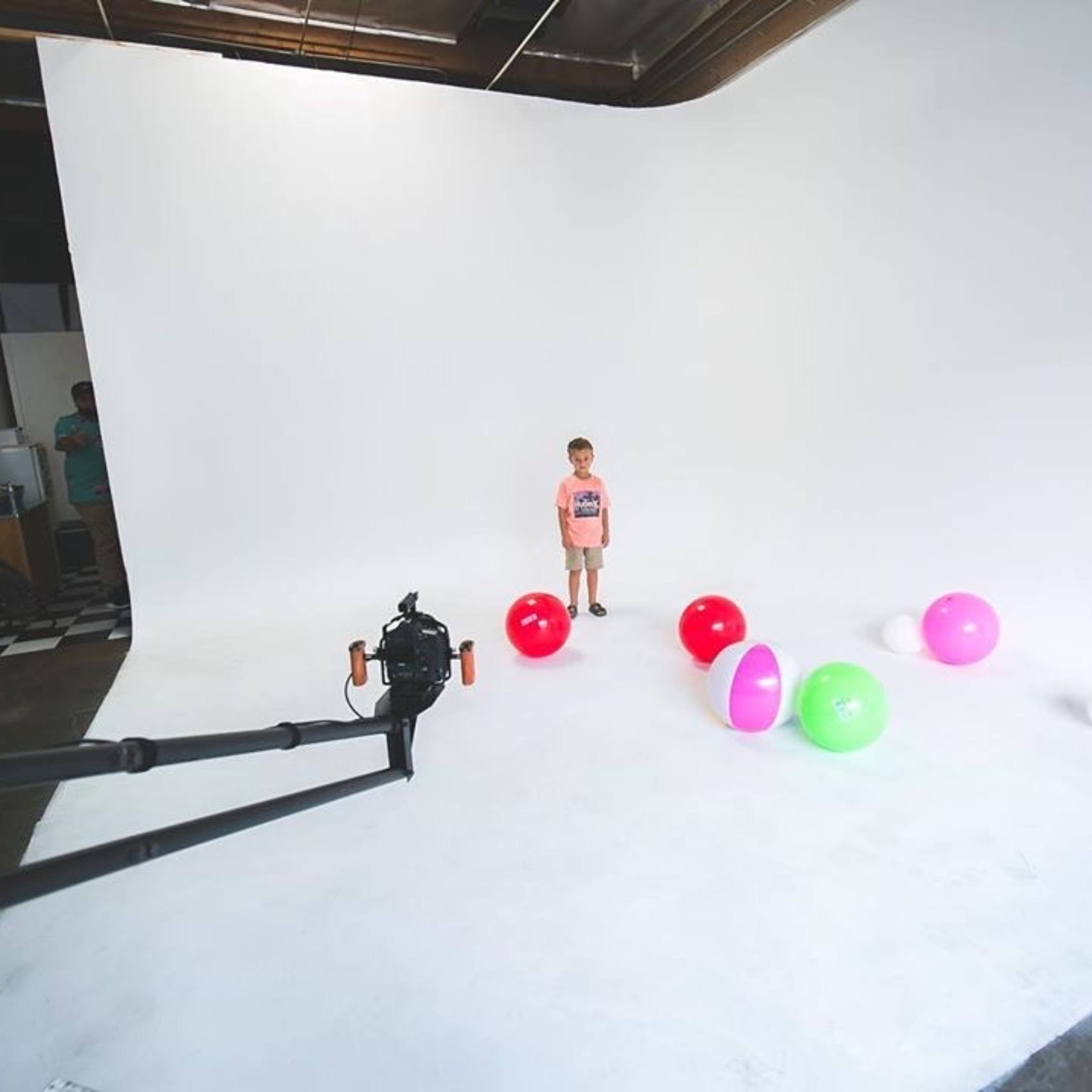 A child stands on a white background surrounded by colorful balls of various sizes.