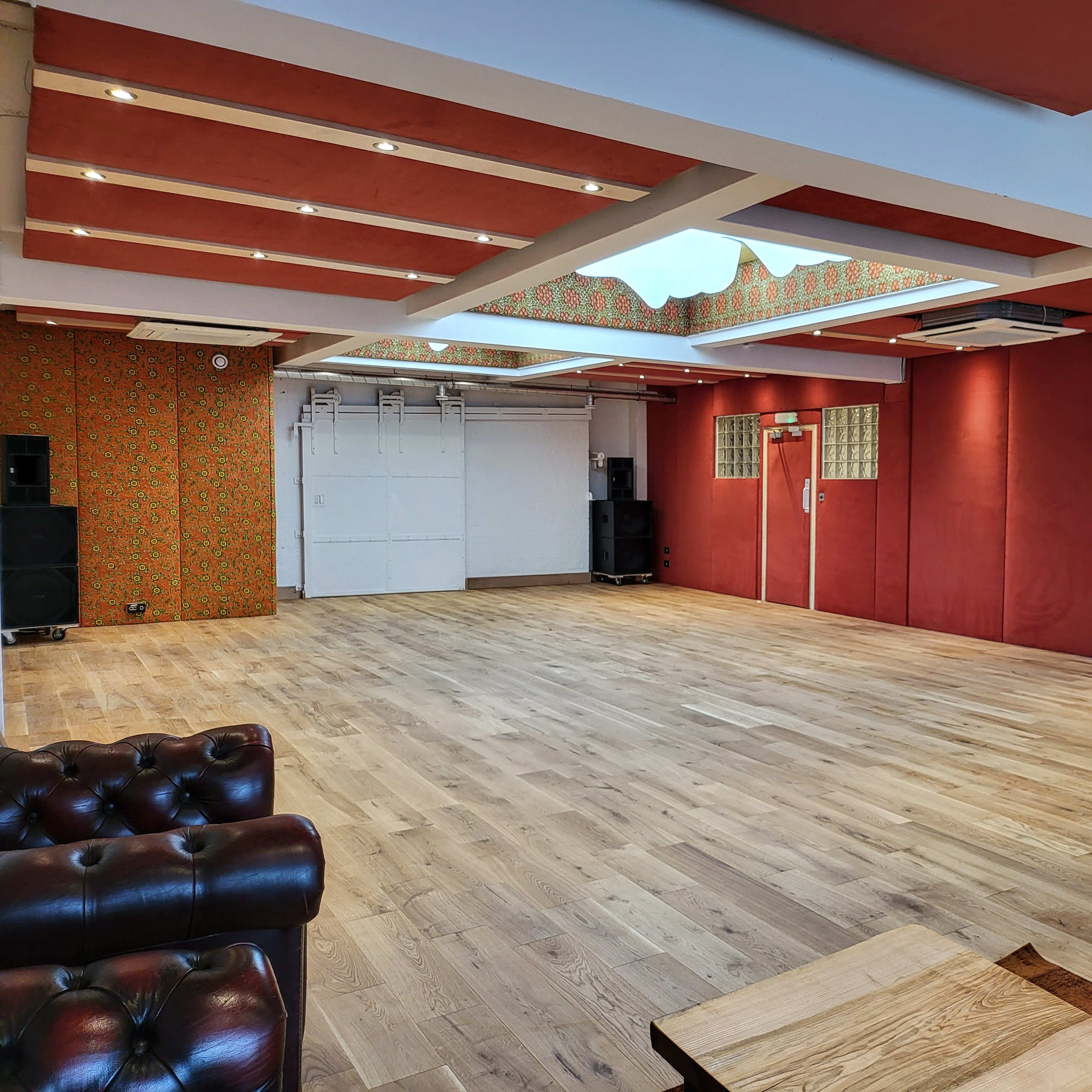 A spacious interior room with wooden flooring, red walls, and a skylight, featuring sound equipment and a lounge area.