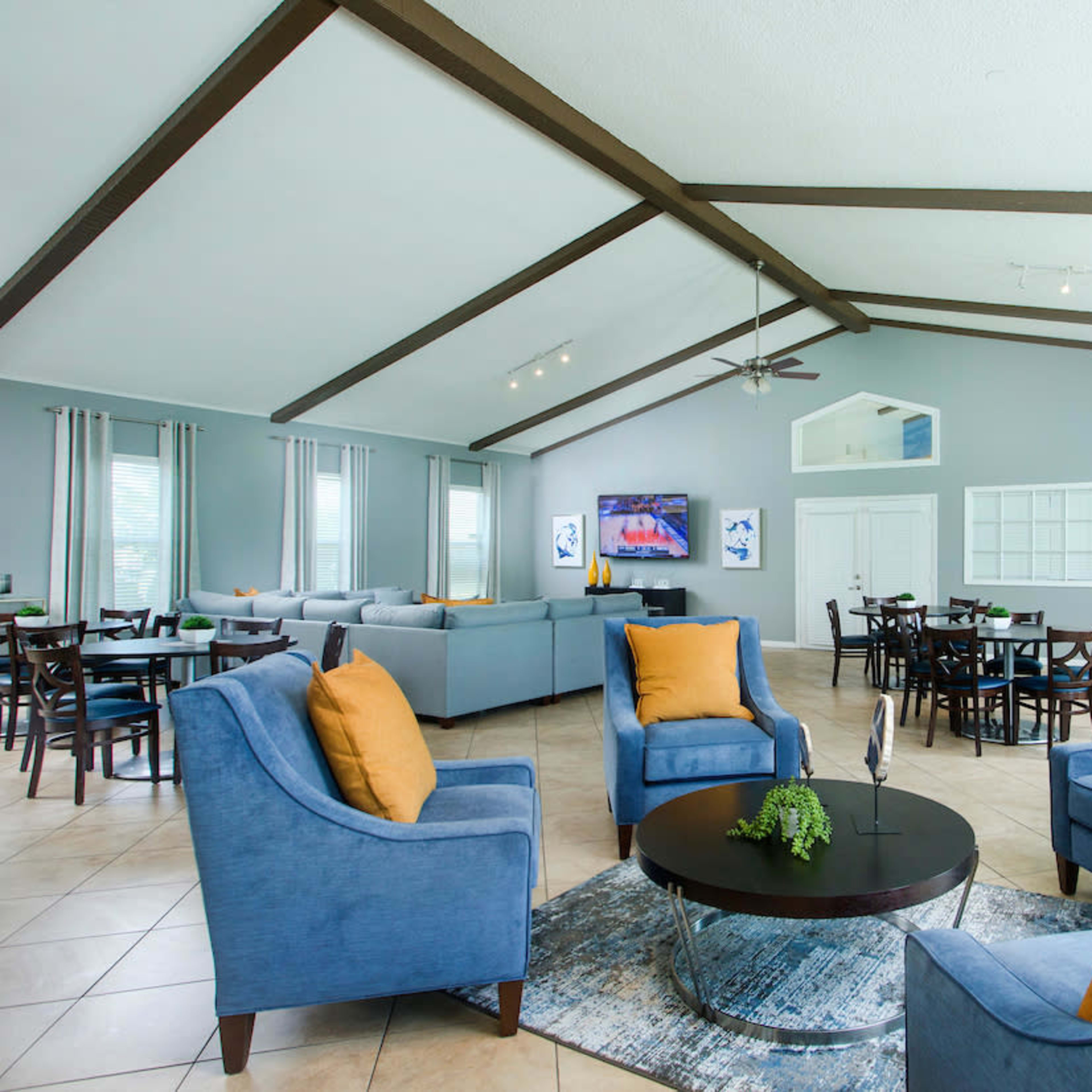 A spacious lounge area with blue armchairs, a round coffee table, and a view of a dining area in the background, featuring tables and chairs.