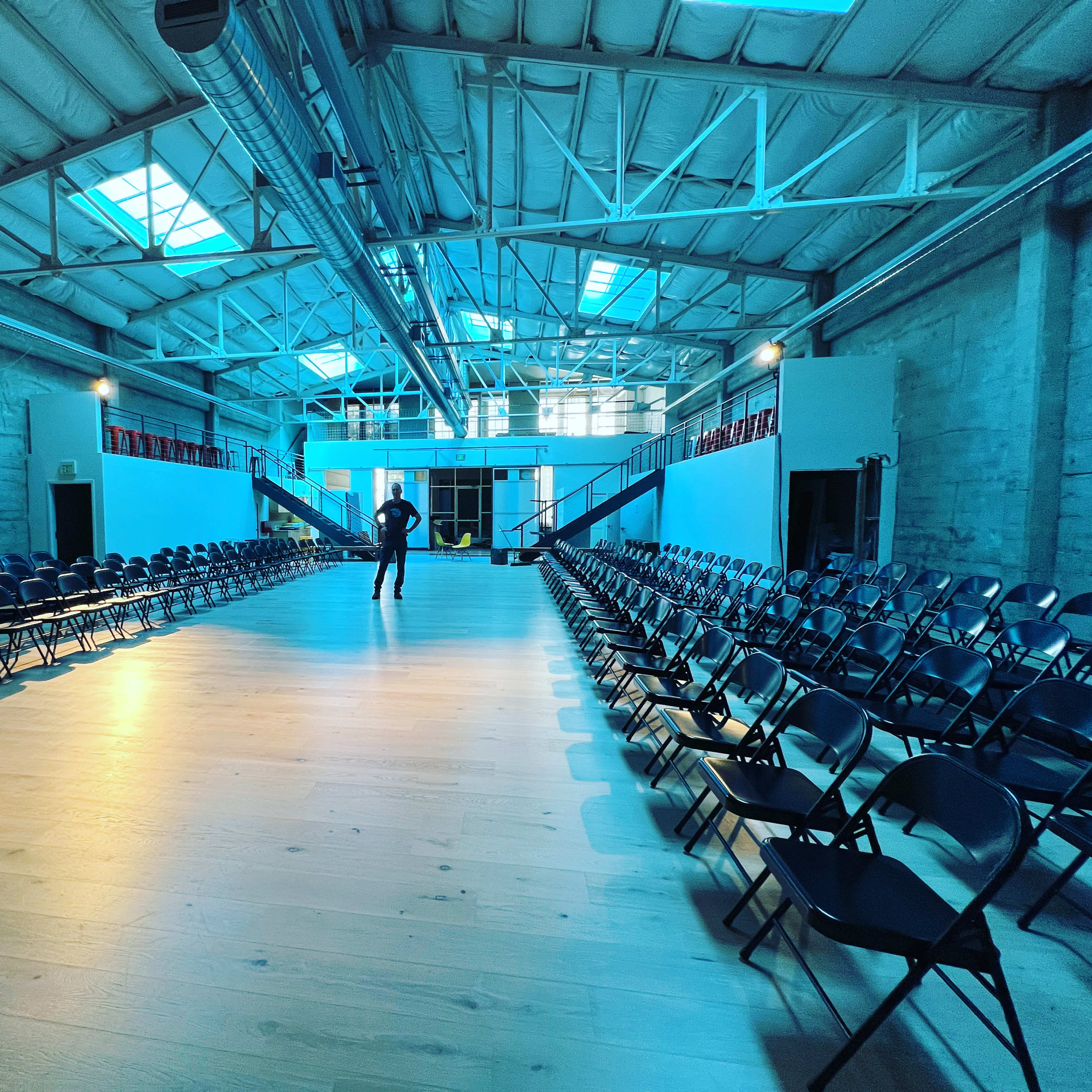 A person stands alone in a spacious venue filled with rows of empty chairs under a skylit ceiling.