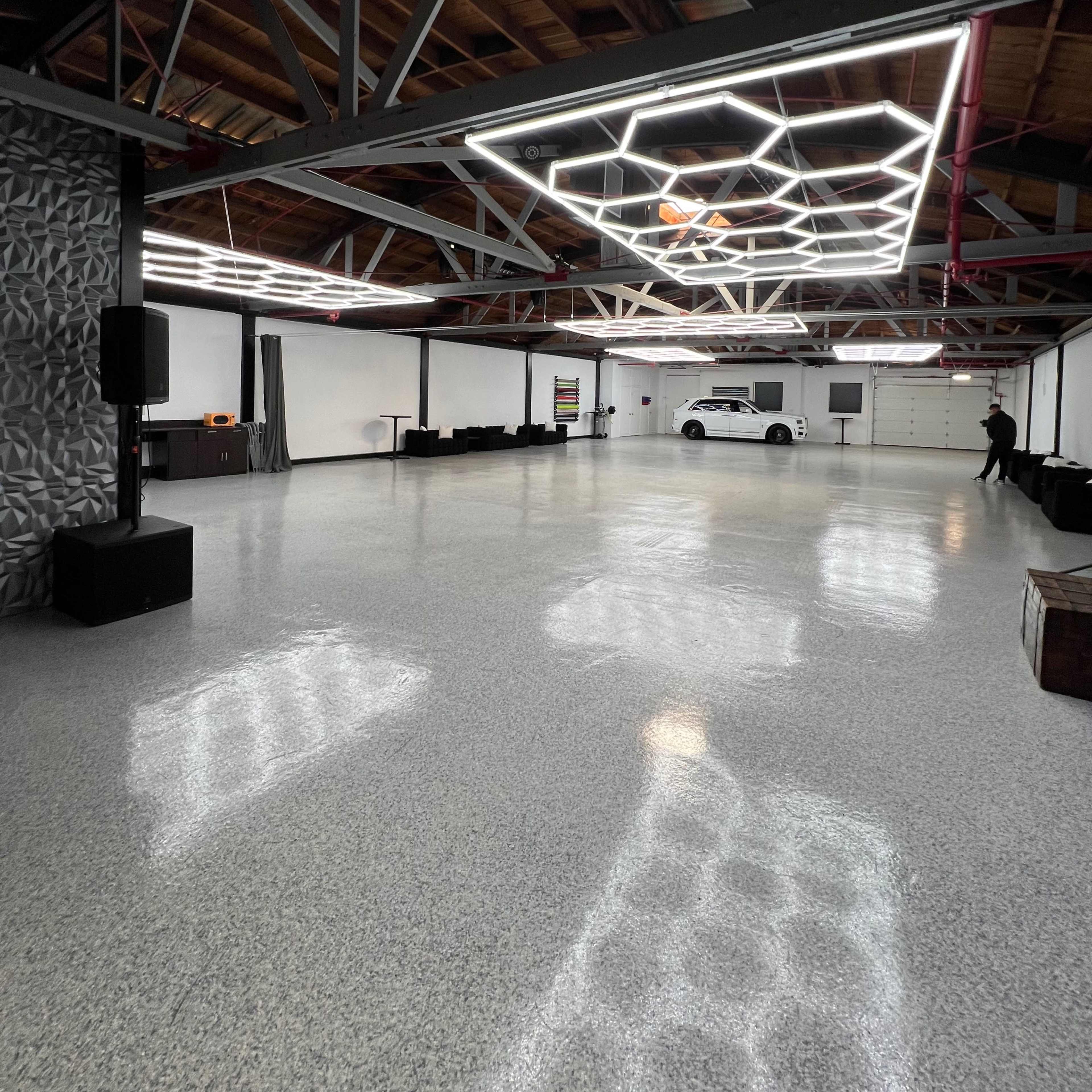 A spacious, modern interior with polished flooring, a geometric light fixture on the ceiling, and minimal furnishings.