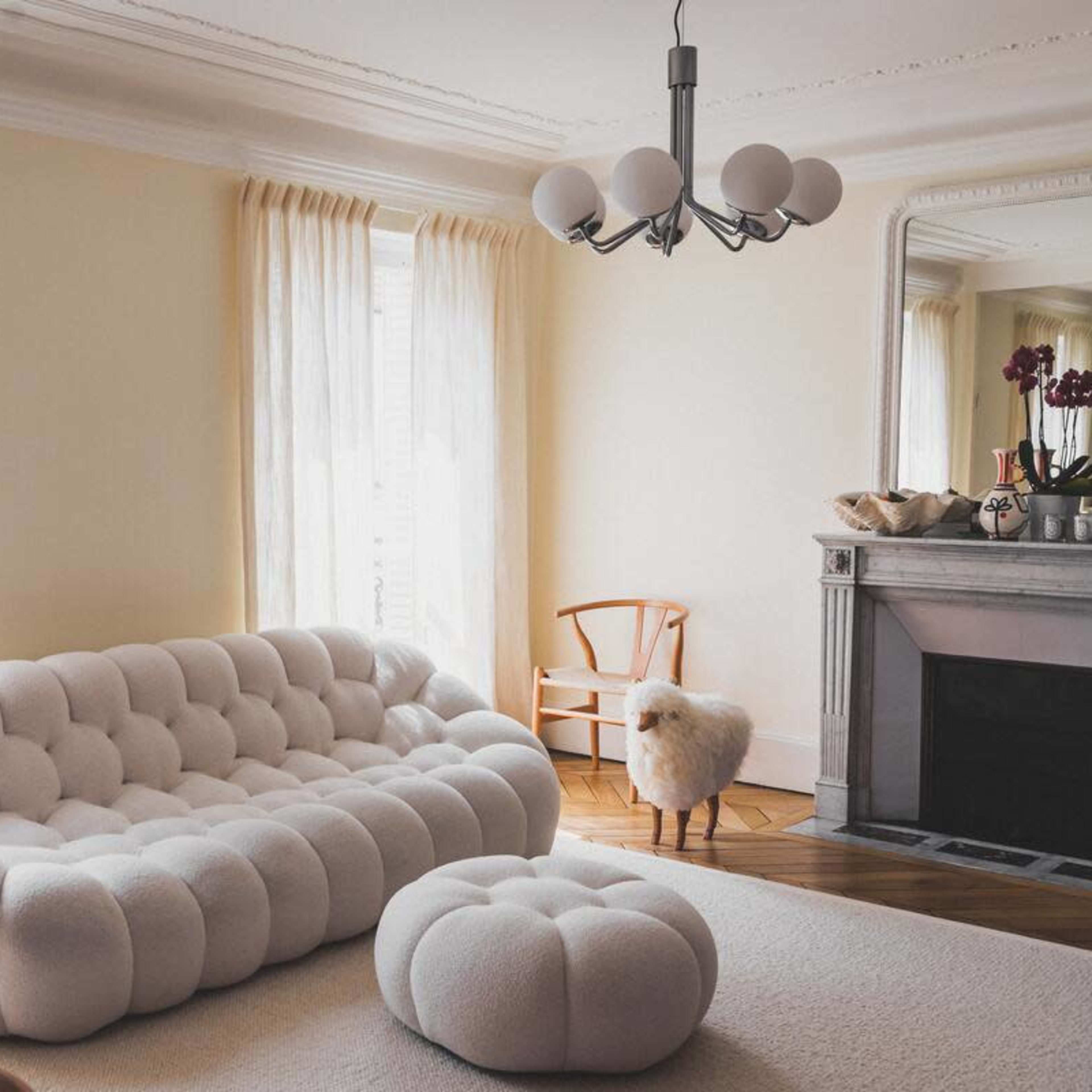 A living room featuring a white, tufted sofa, a matching ottoman, a wooden chair, and a fireplace with a decorative mantel.