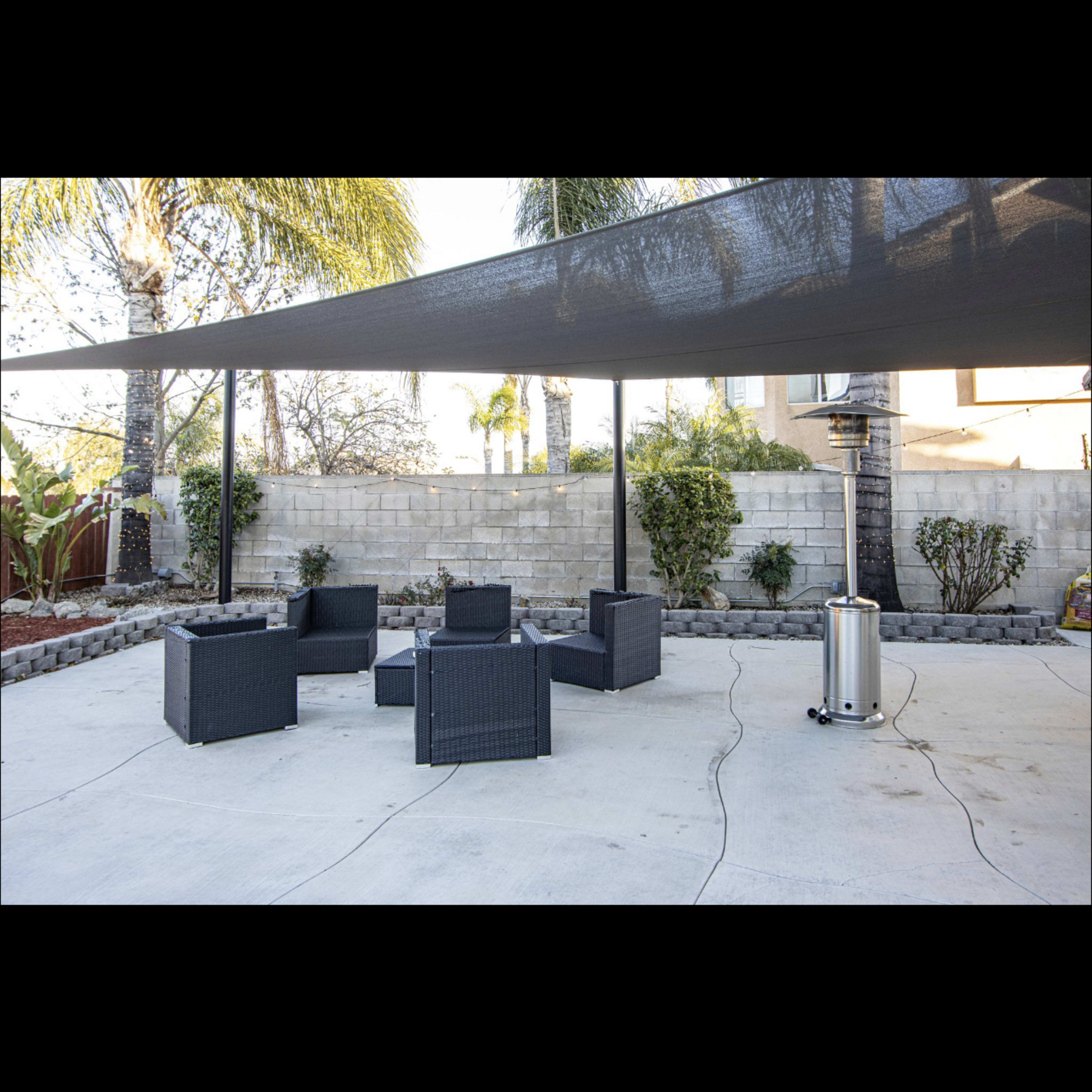 A modern outdoor seating area features several black wicker chairs and a table beneath a shaded canopy on a concrete patio.