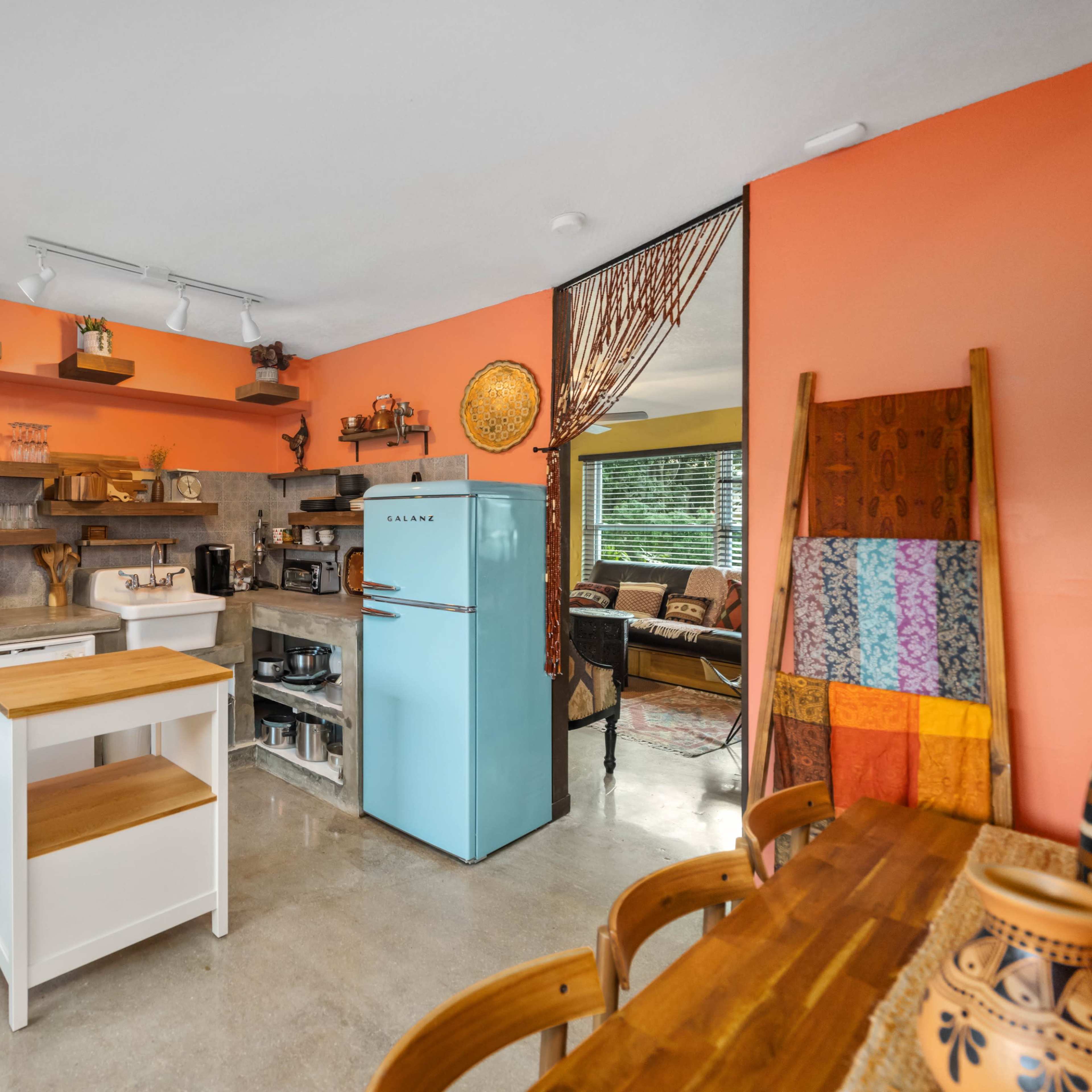 A modern kitchen with orange walls, a blue refrigerator, a central wooden island, and various cooking appliances and shelves.