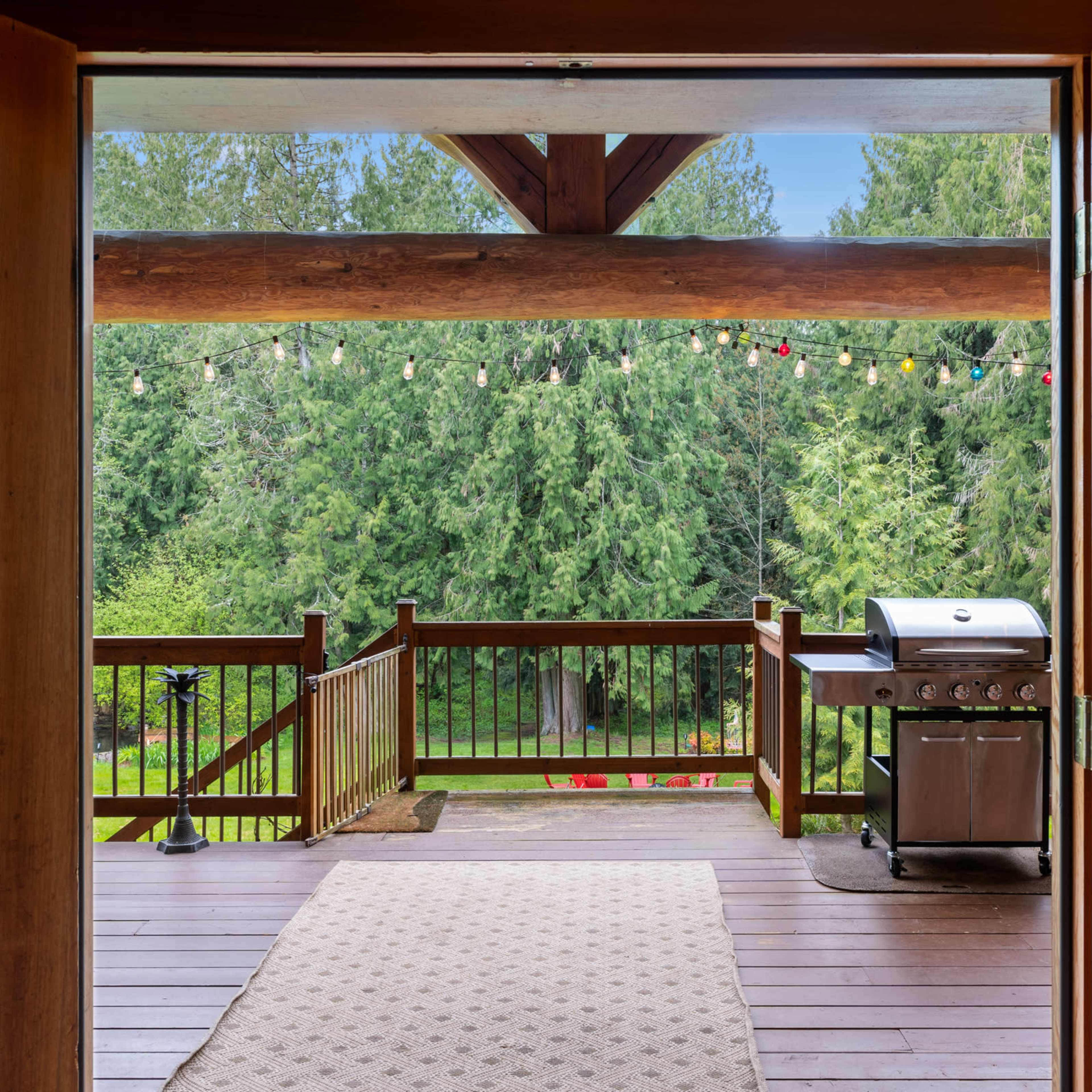 A wooden deck with a barbecue grill and a view of a forested area, framed by large sliding glass doors.