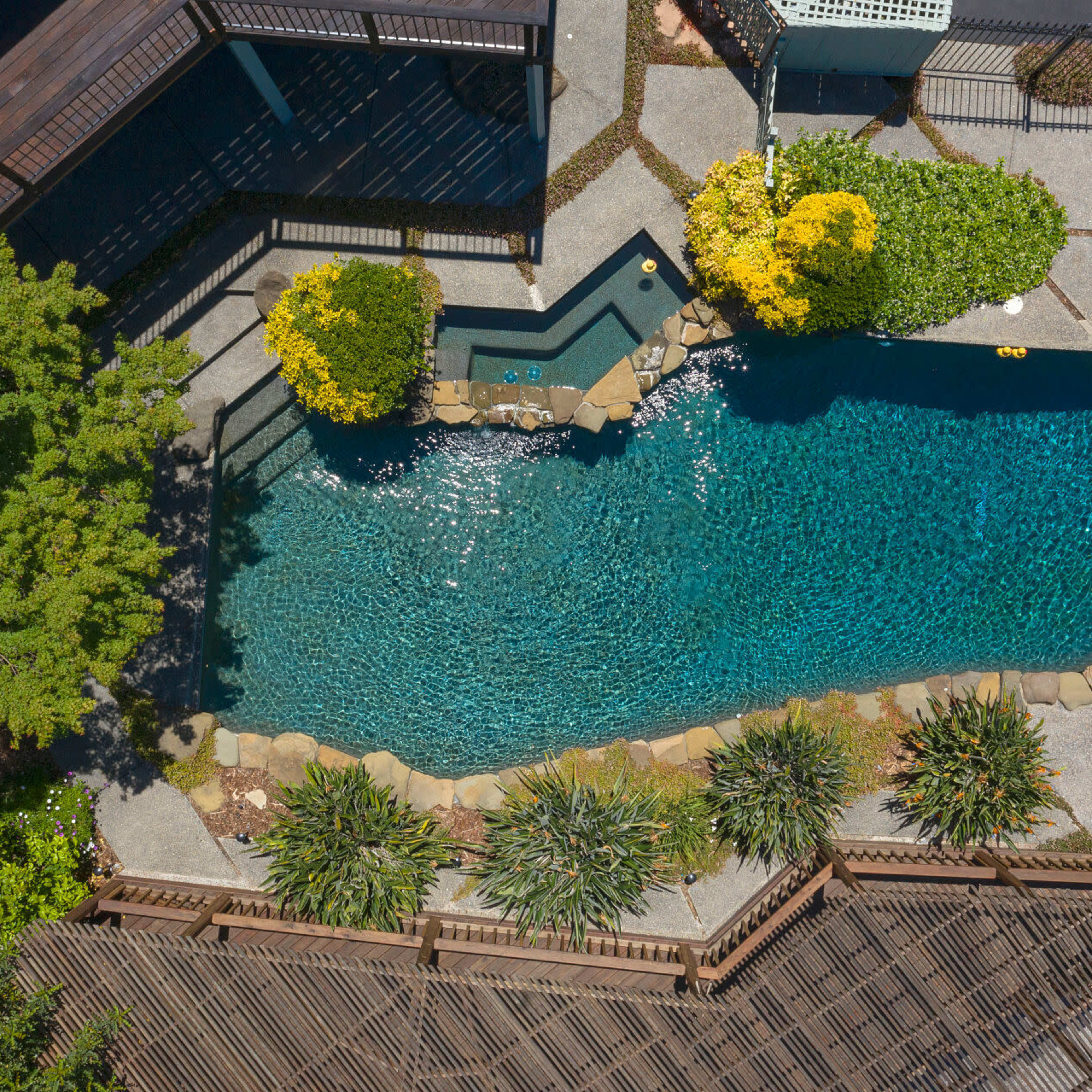 An aerial view showcases a landscaped backyard featuring a swimming pool surrounded by stone edging and greenery.