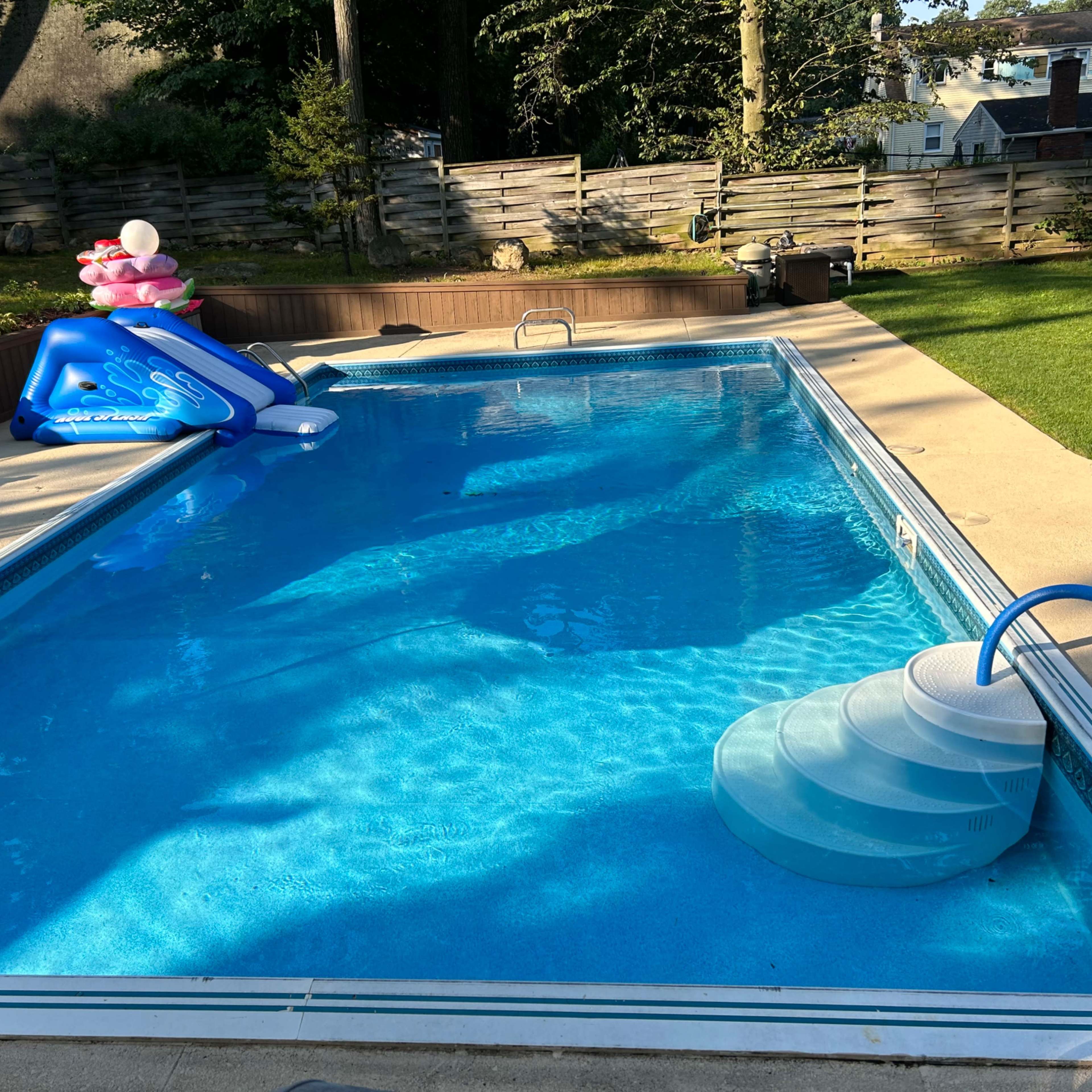 A clean swimming pool is surrounded by a patio area, featuring blue water slides and a slide entry.