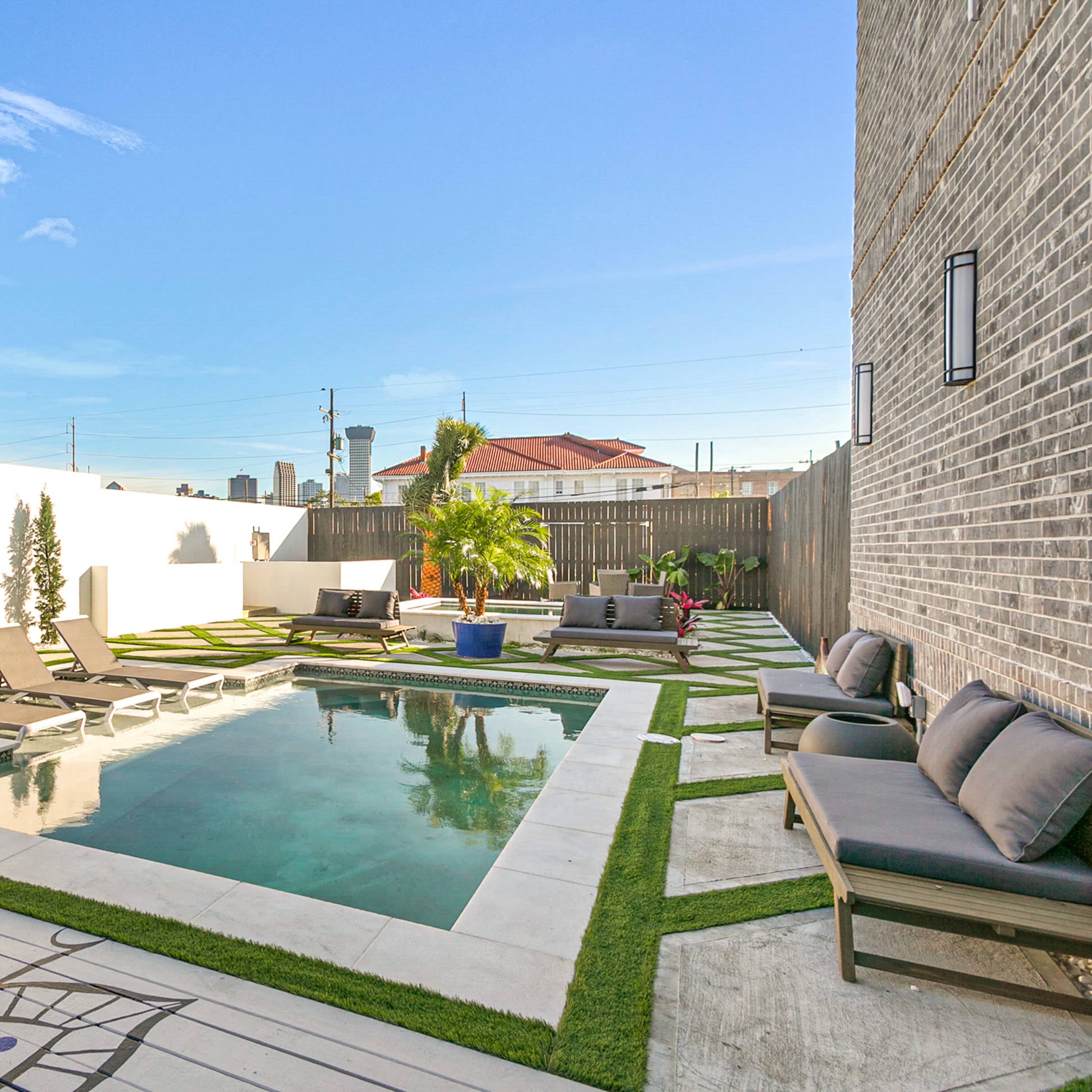 A modern backyard featuring a rectangular swimming pool surrounded by lounge chairs, decorative plants, and stone pathways.