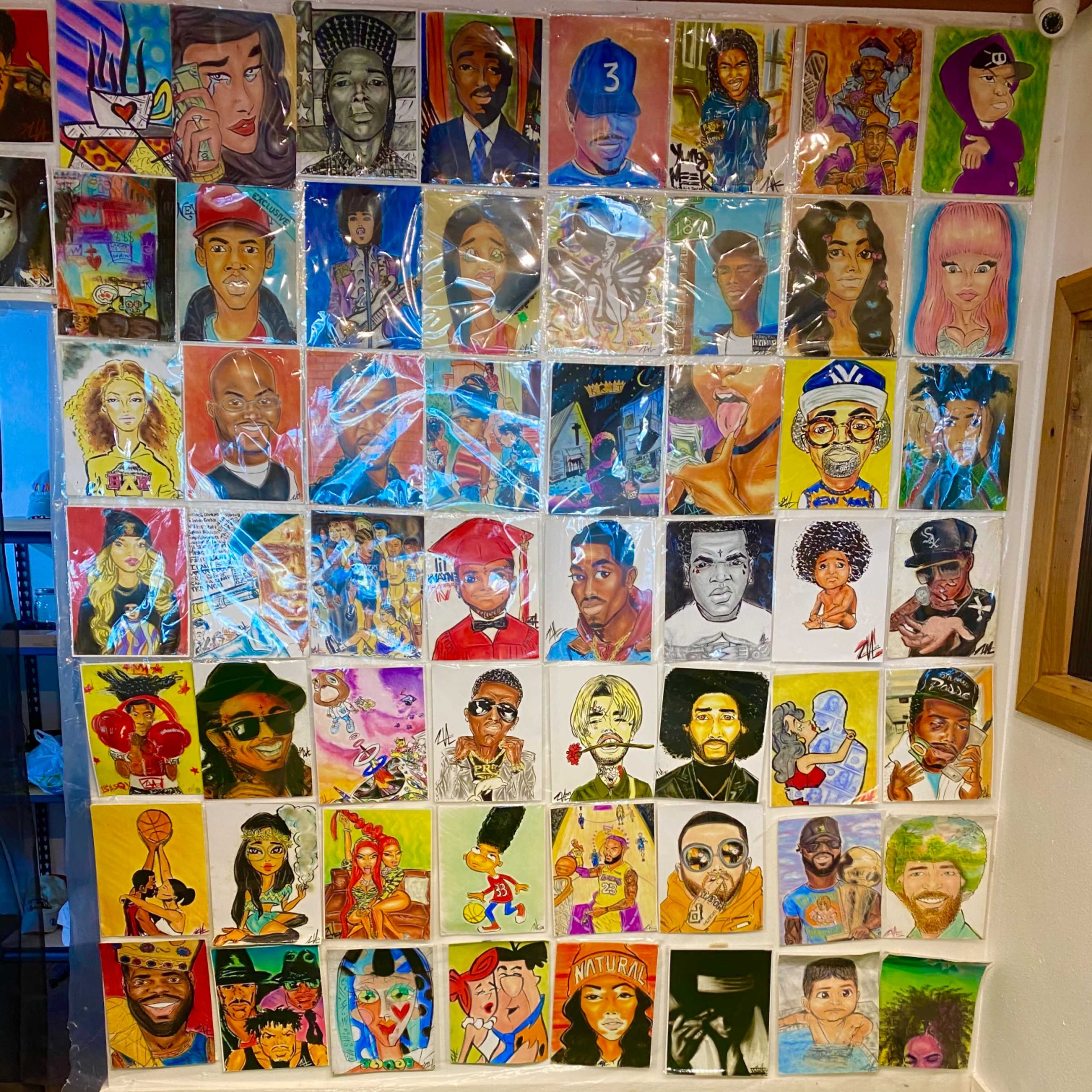 A wall covered with colorful portraits and artwork featuring various people and characters, arranged in a grid pattern.