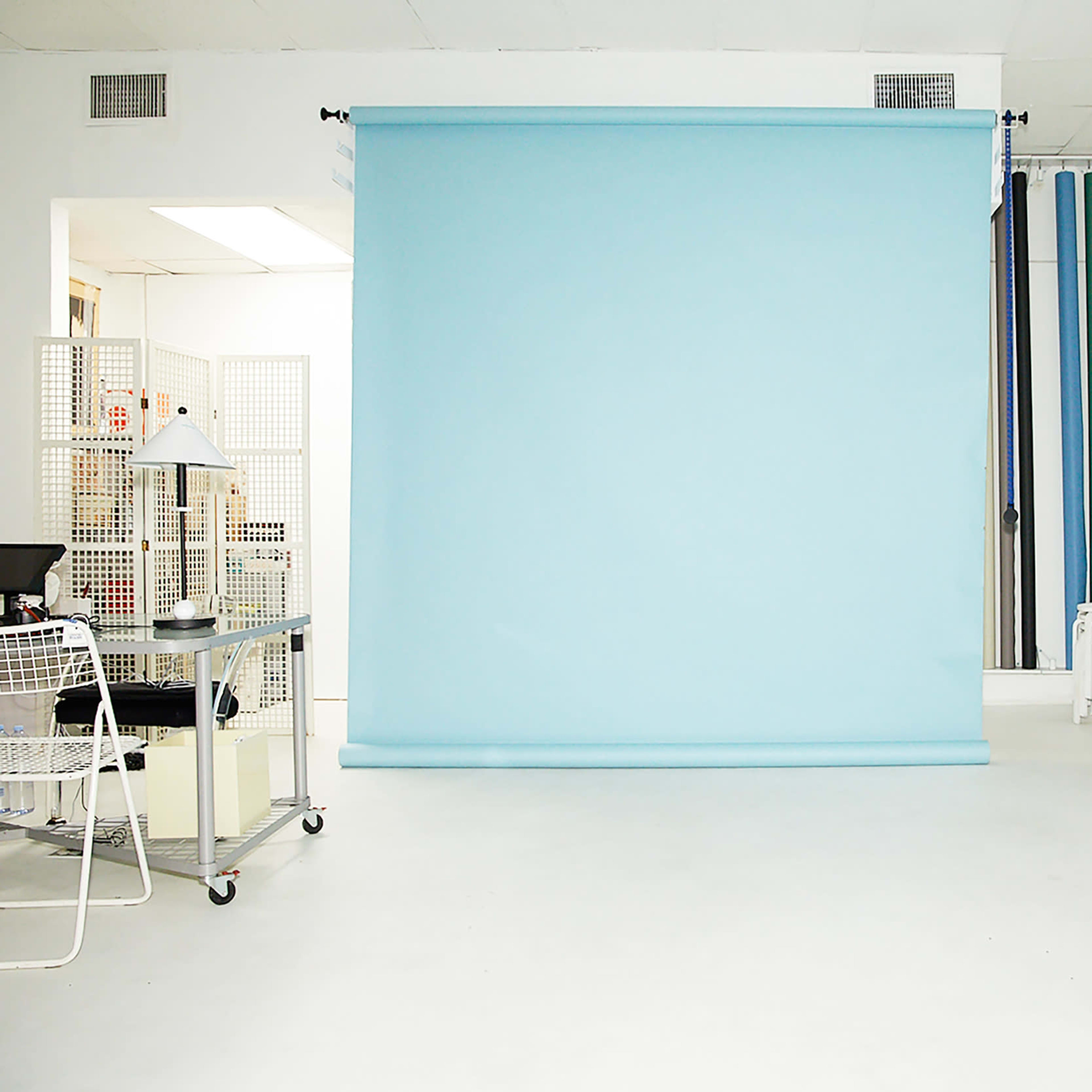 A bright white room with a pale blue backdrop, a small blue table, and a workstation featuring a lamp and various studio equipment.