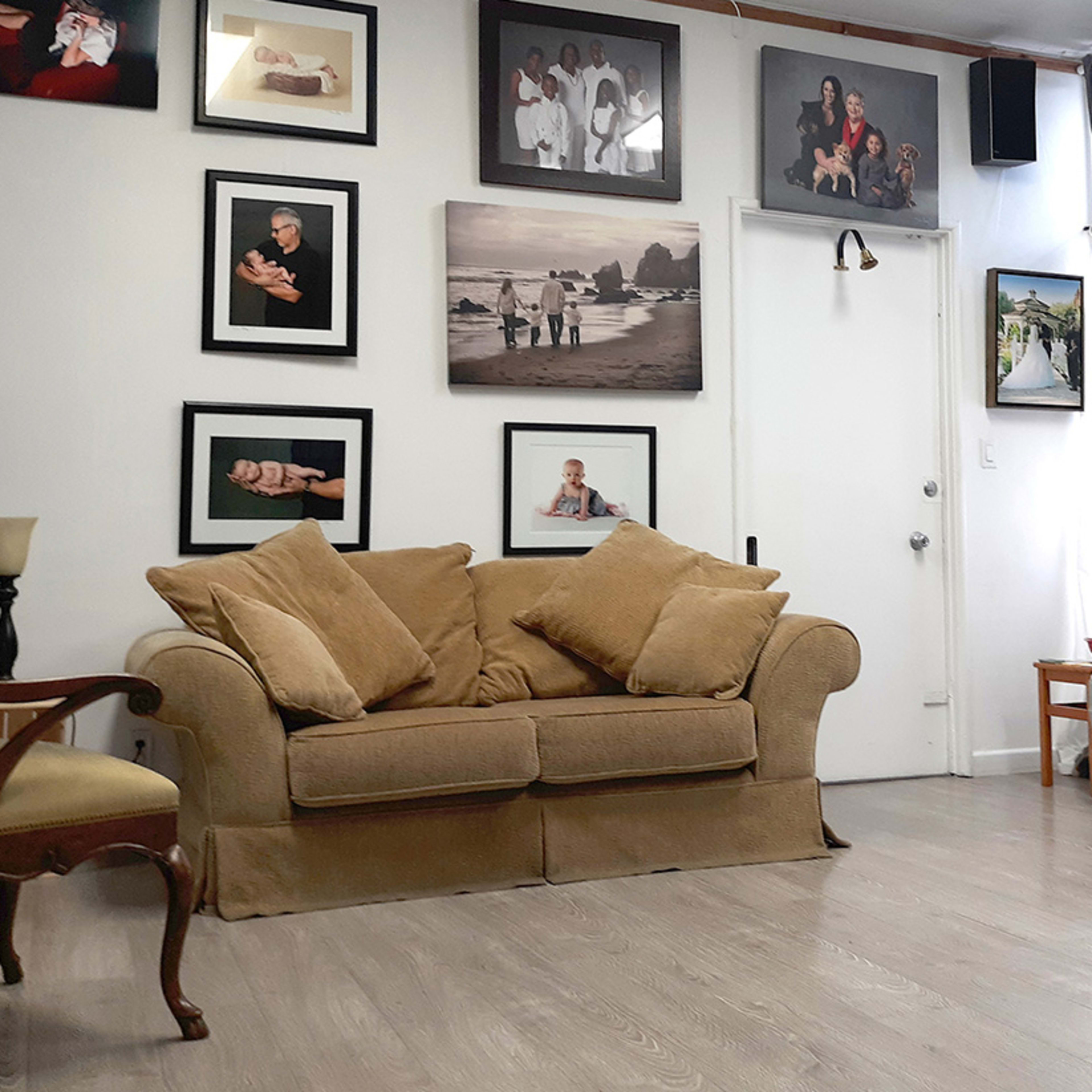 The scene features a living room with a beige couch, various framed photographs on the walls, and two chairs opposite each other.