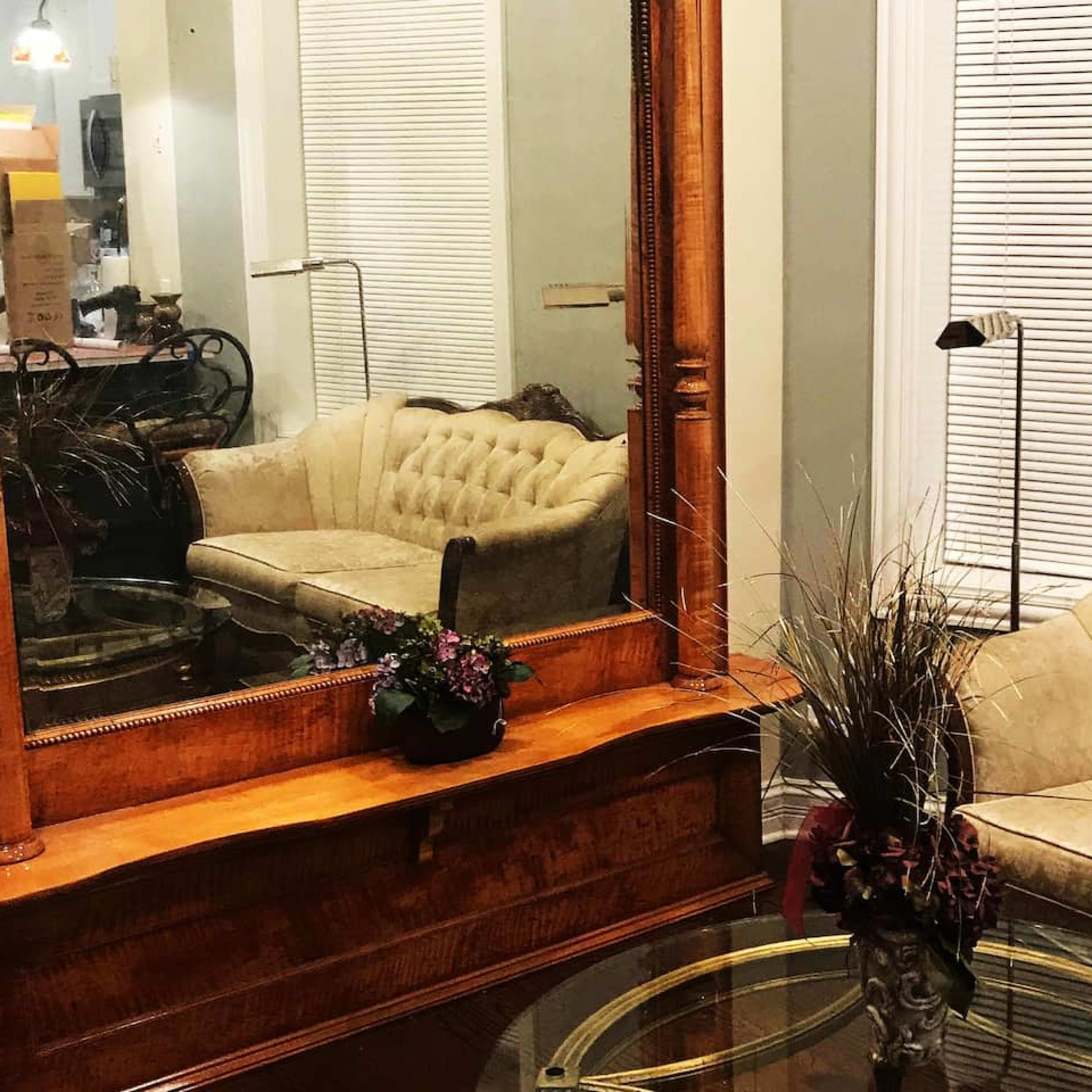 A cozy sitting area featuring a tufted beige sofa, a round glass coffee table, and a large wooden mirror reflecting the space.