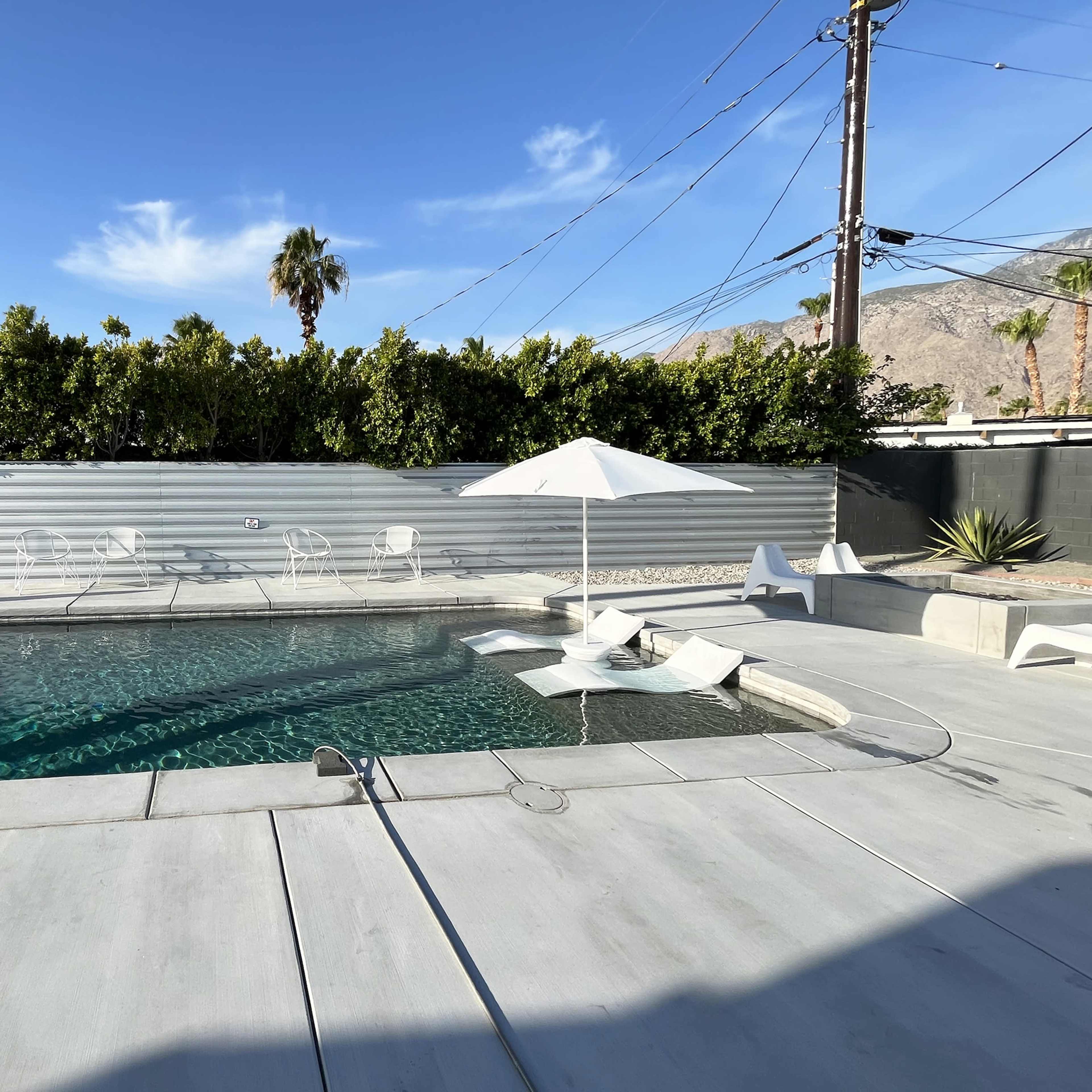 A pool area features a rectangular swimming pool surrounded by concrete, with lounge chairs and an umbrella, and palm trees in the background.