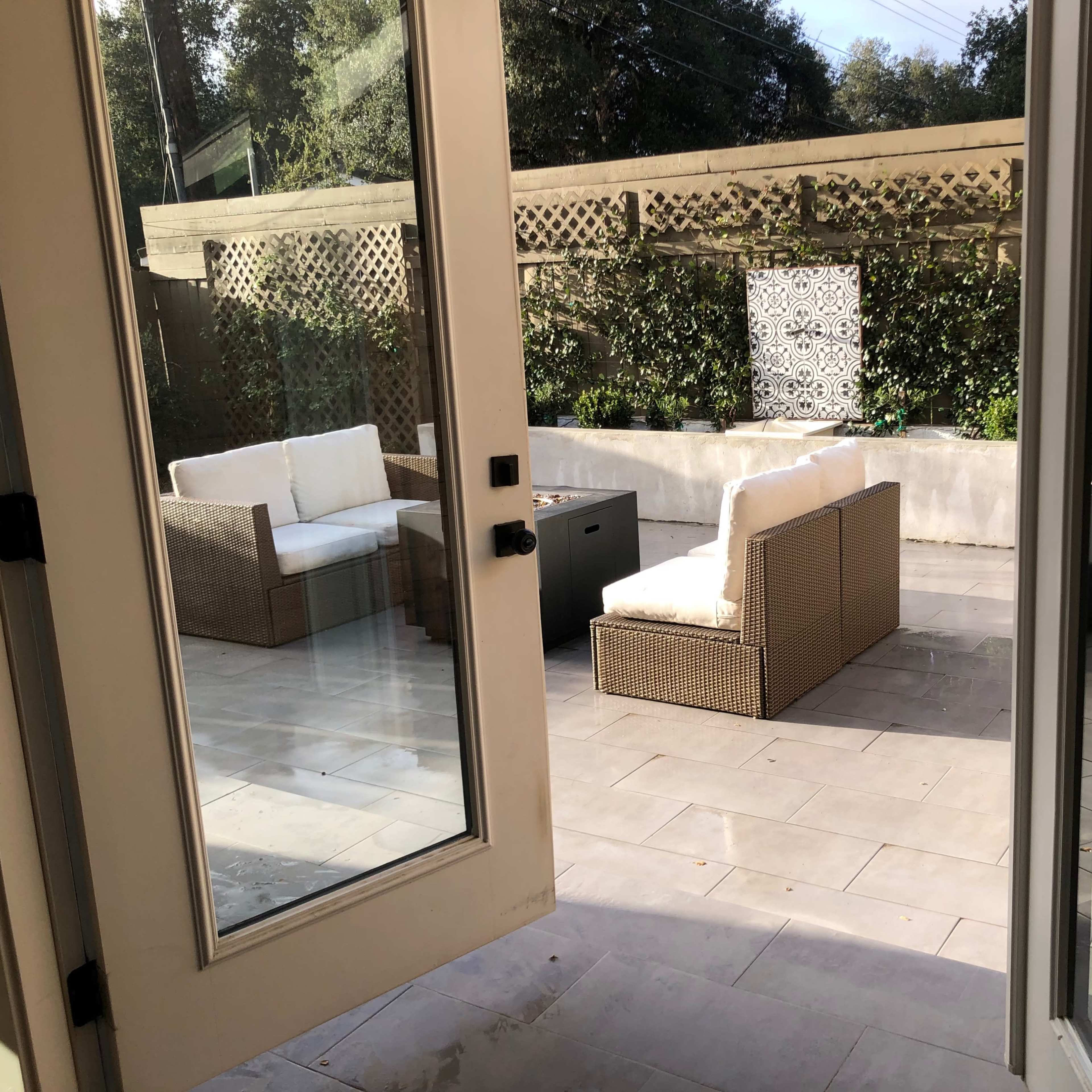 An outdoor patio with two wicker chairs and a small table, framed by glass doors.
