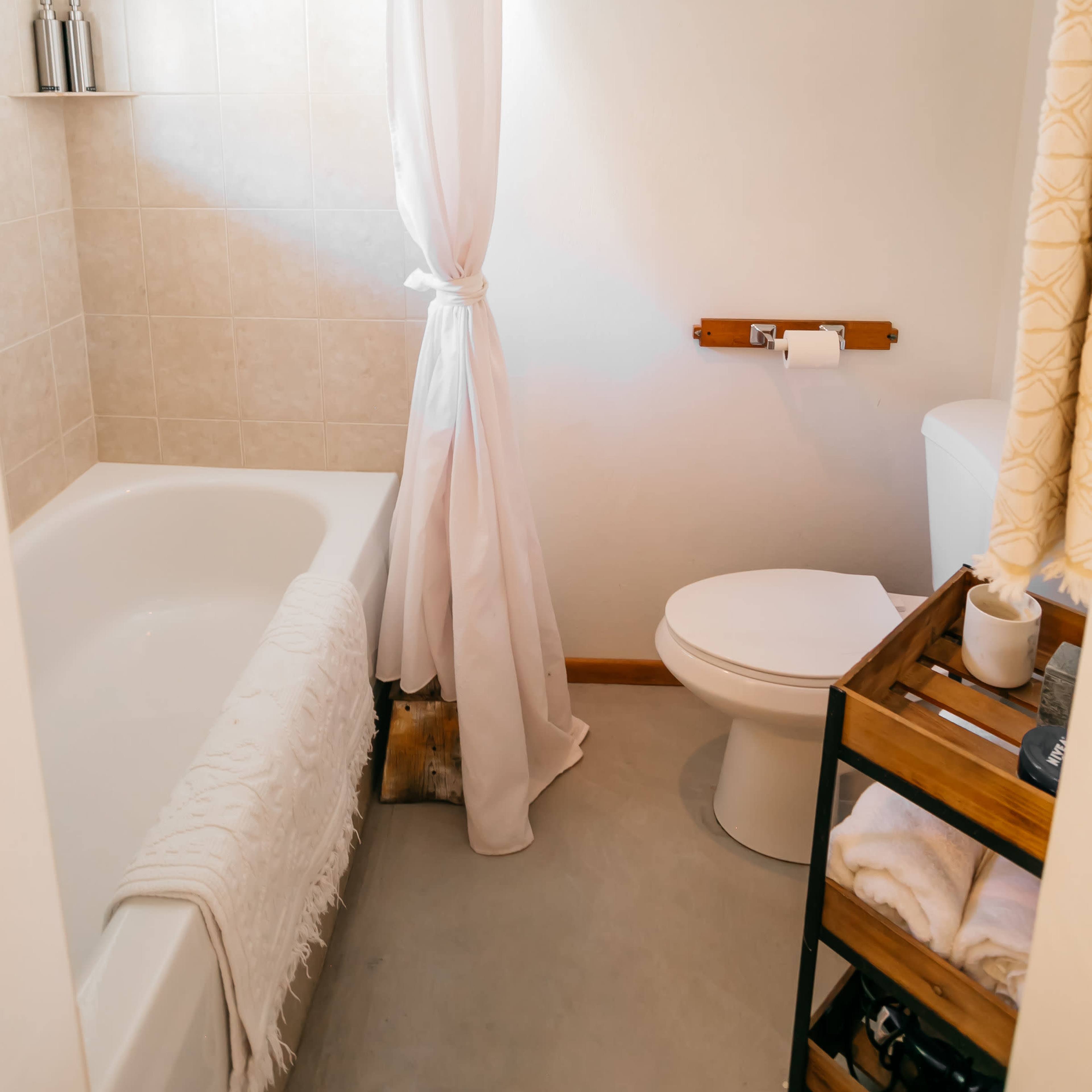The bathroom features a bathtub with a shower curtain, a toilet, and a wooden rack holding toiletries.