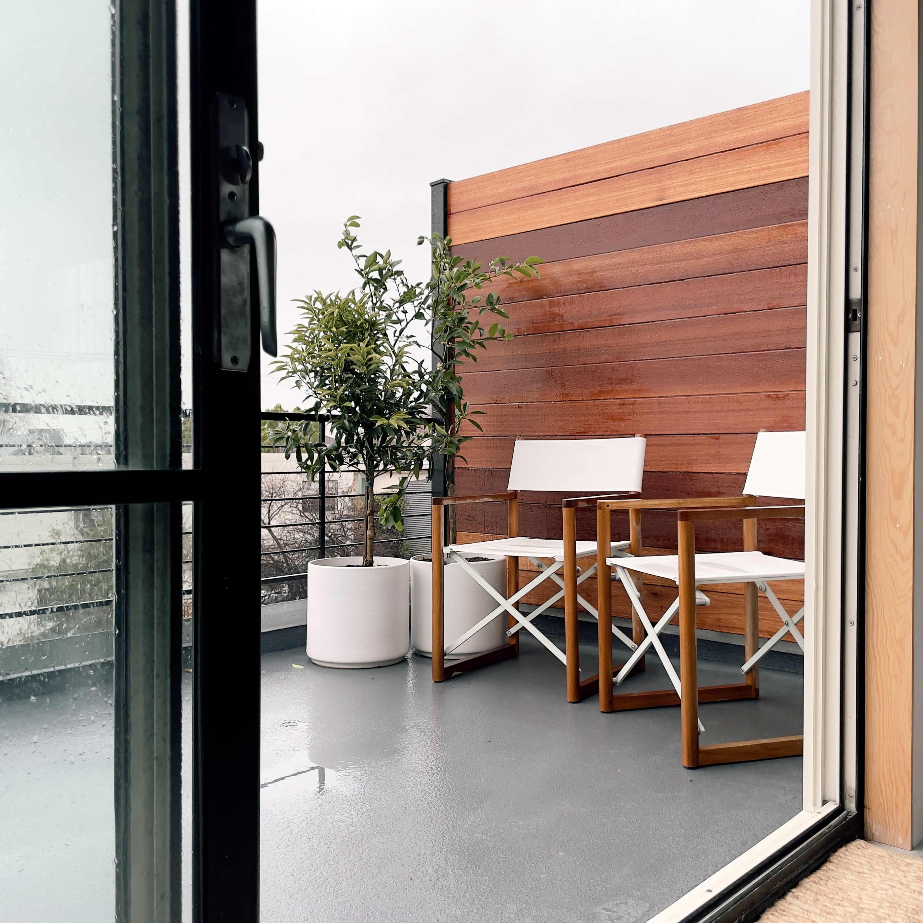 A balcony features two white chairs and a potted plant against a wooden wall.