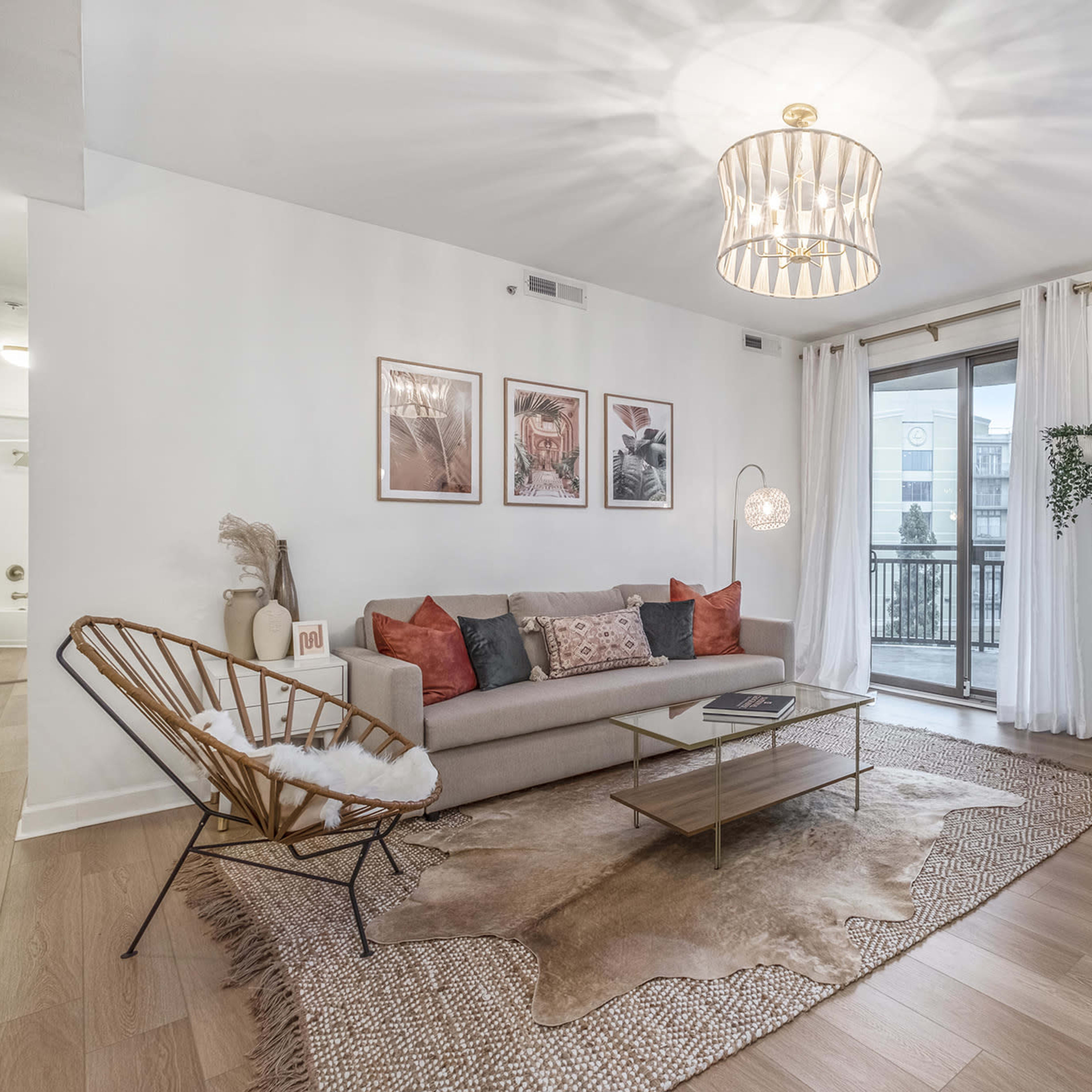 A modern living room features a sofa with decorative pillows, a coffee table, a large TV, a light fixture, and sliding glass doors opening to a balcony.