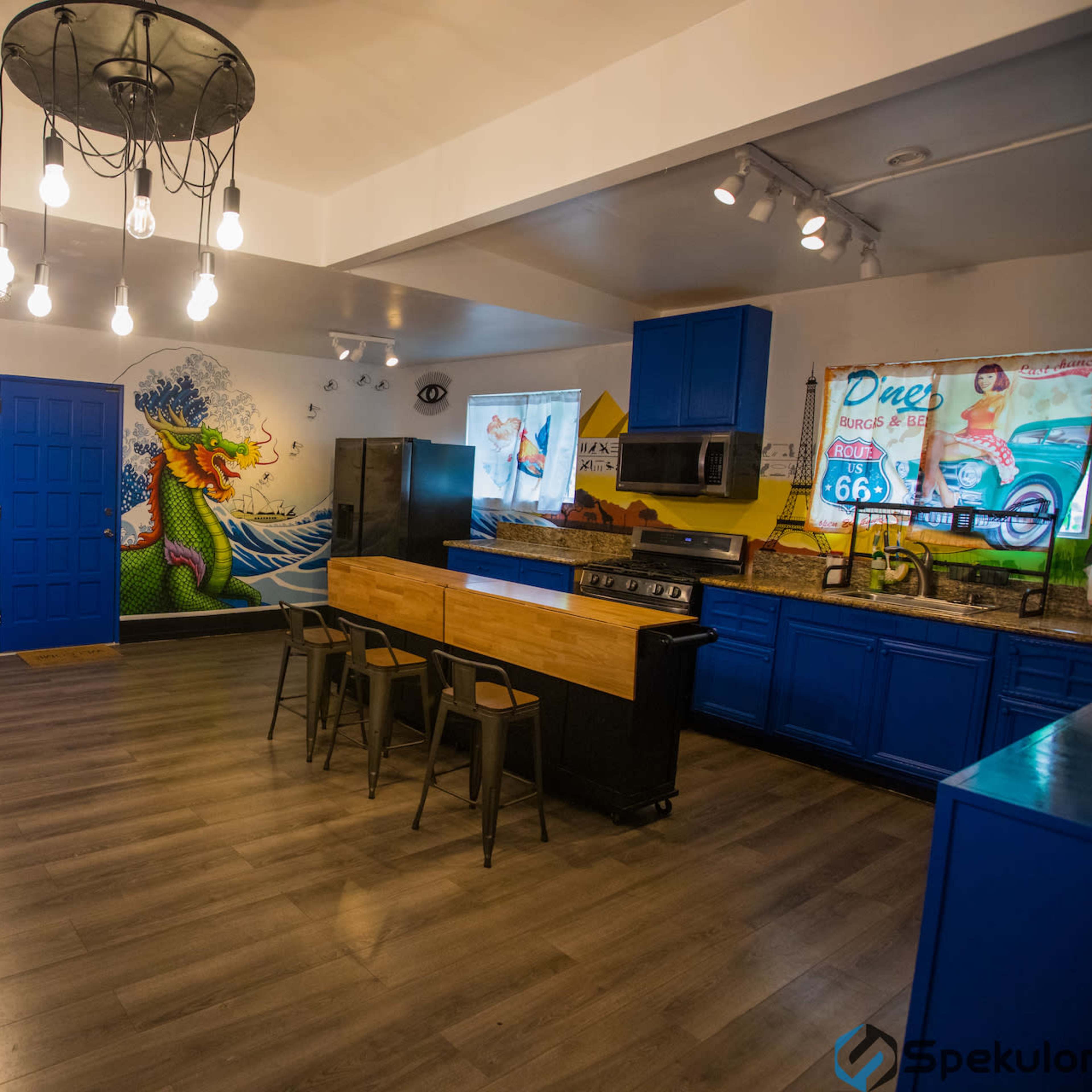 A modern kitchen and dining area featuring blue cabinetry, a mural of a wave and a woman on the wall, and a central island with seating.