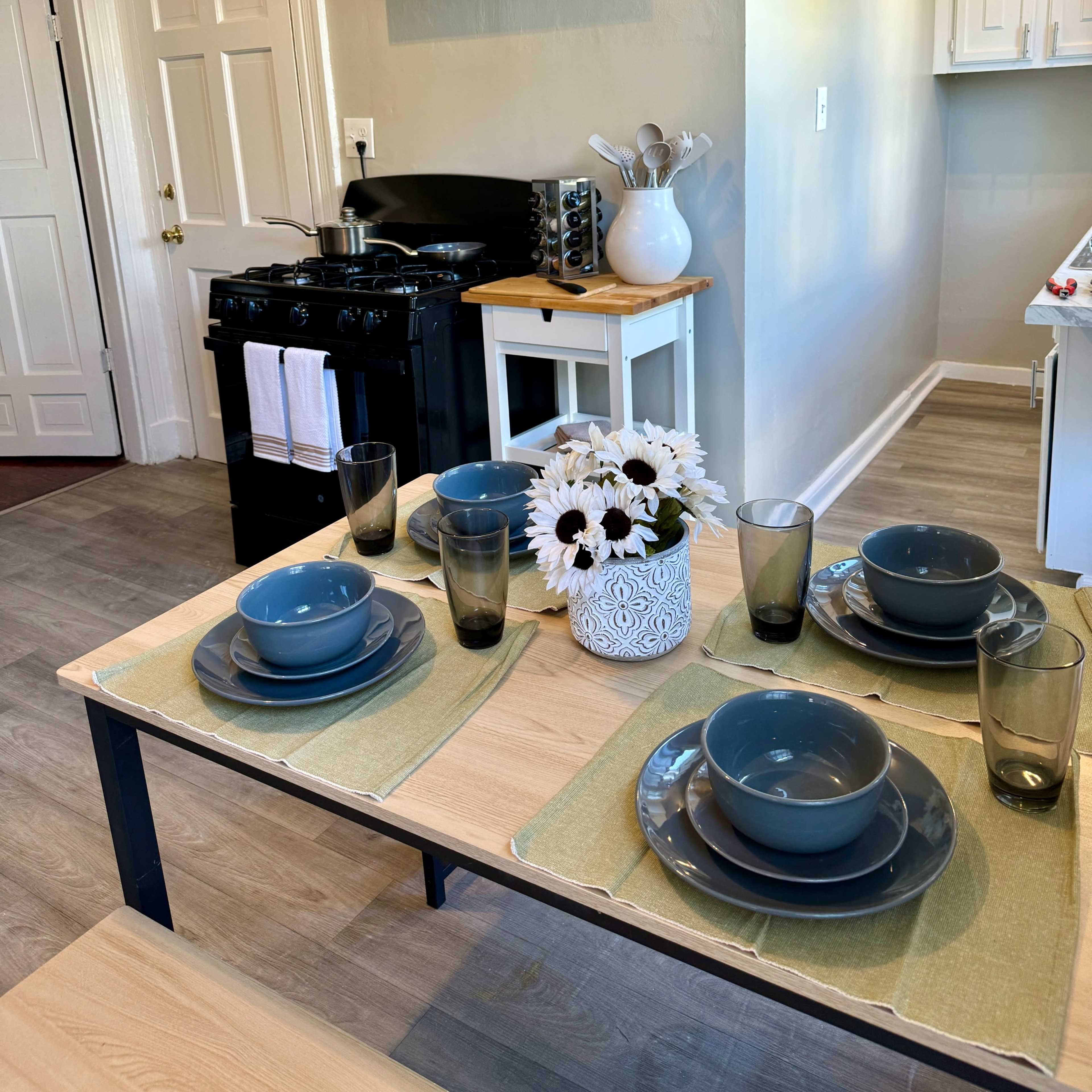 A kitchen with a dining table set for four, featuring plates and glasses, next to a stove and cabinets.